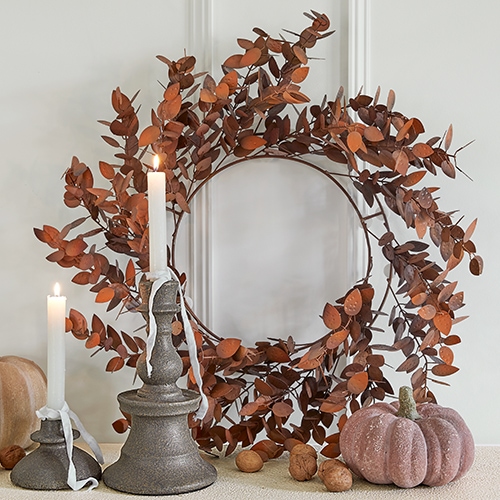 Decoratieve krans van roestkleurige metalen bladeren met twee kaarsen en decoratieve pompoen op tafel