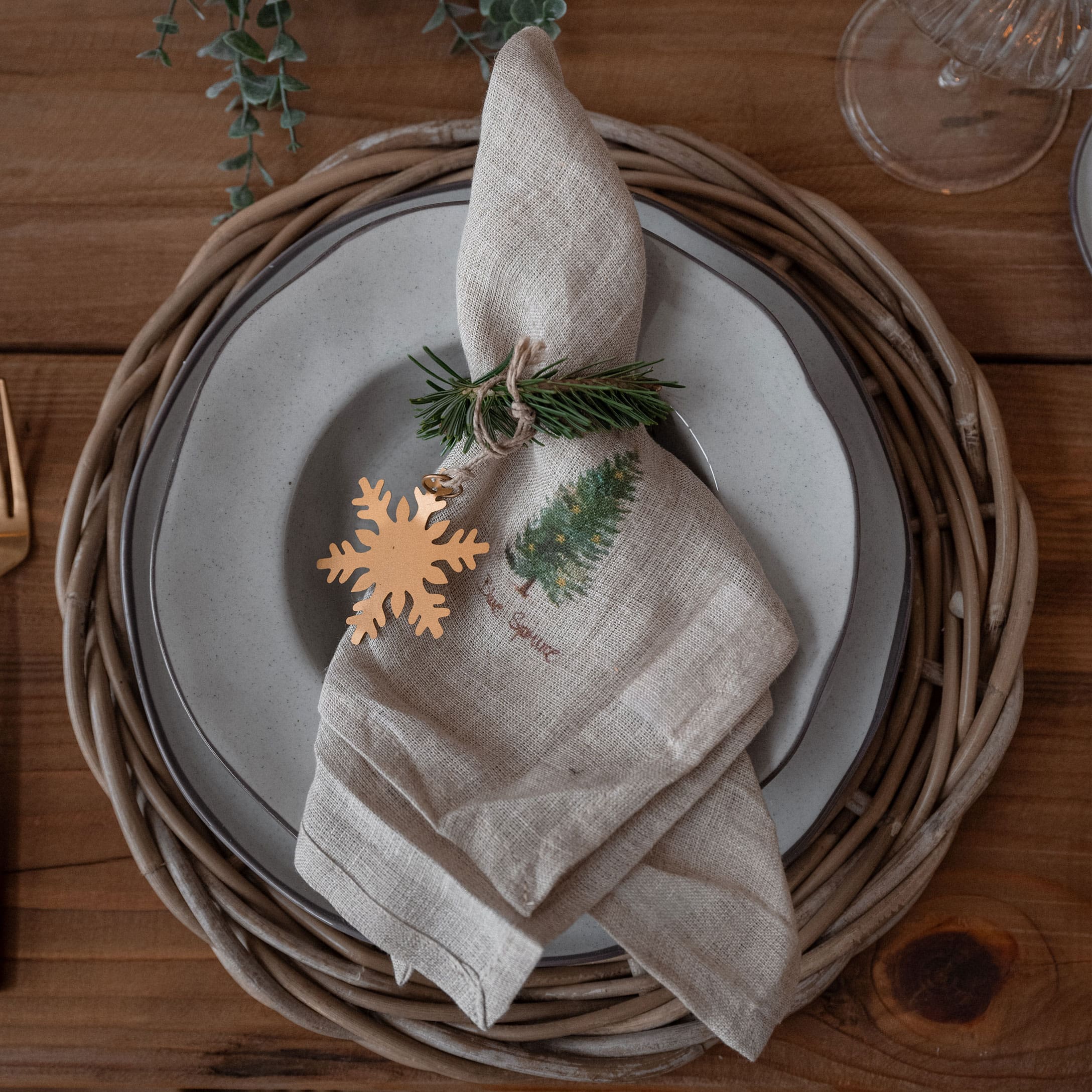 Kersttafel met linnen servet in natuurlijke kleur, versierd met groene tak en gouden sneeuwvlokhanger
