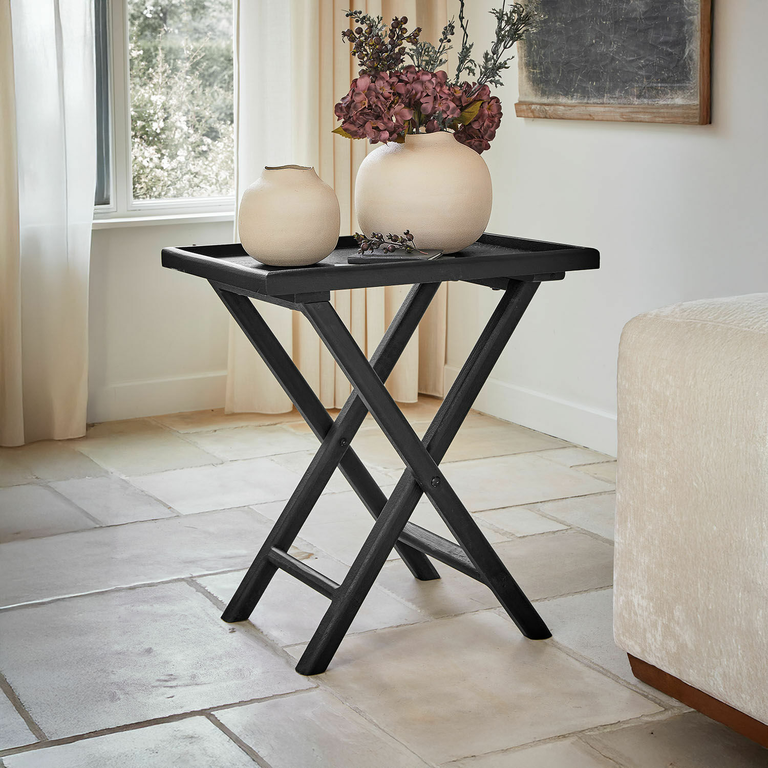 Zwart inklapbaar houten tafeltje met twee beige vazen en bloemendecoratie in lichte woonkamer