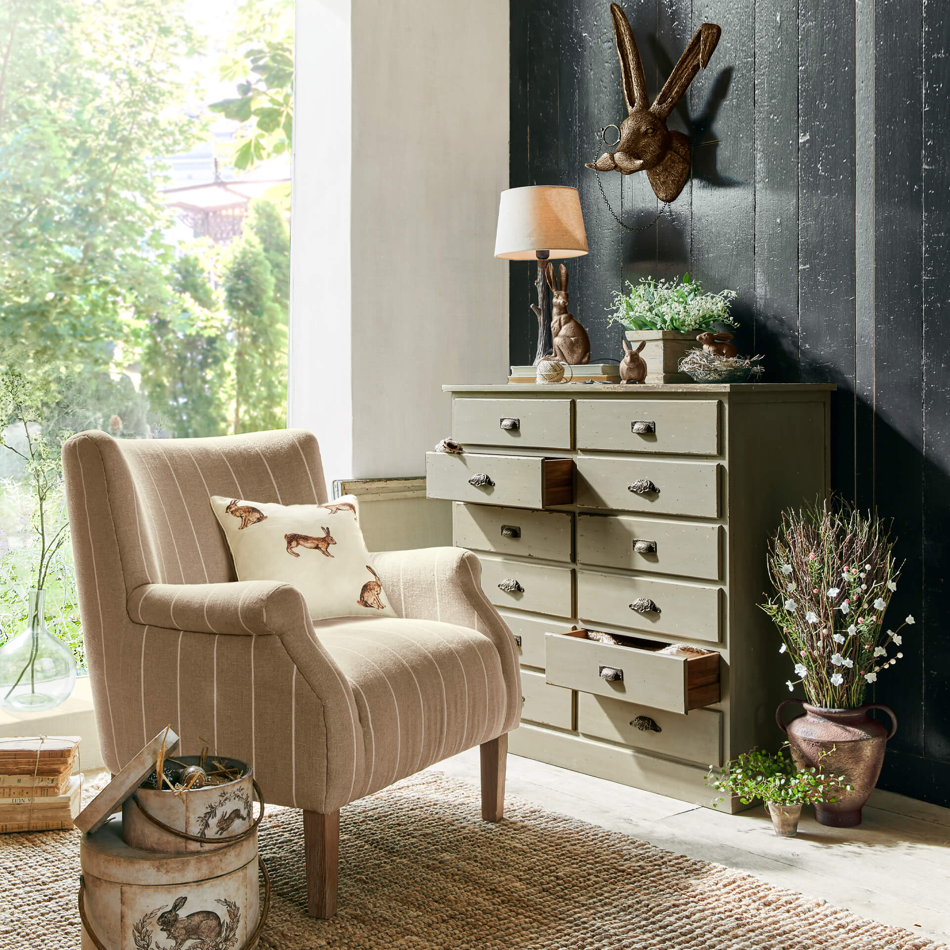 Beige stoffen fauteuil met kussen met konijnmotief naast groene ladekast en rustieke decoratie