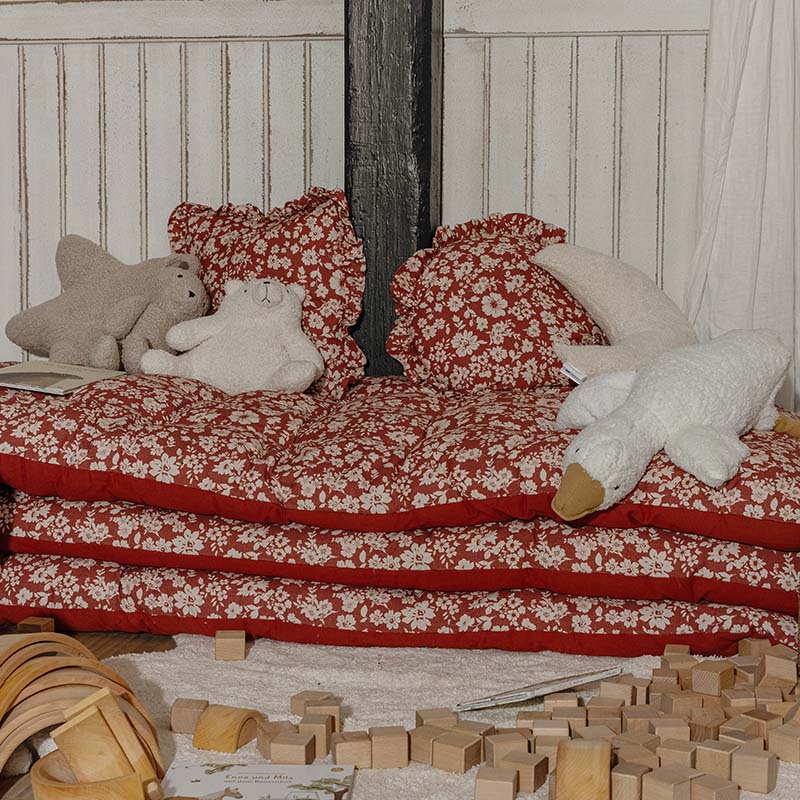 Rode bloemenkussens en matrassen met knuffels in een kinderhoek met houten blokken om mee te spelen
