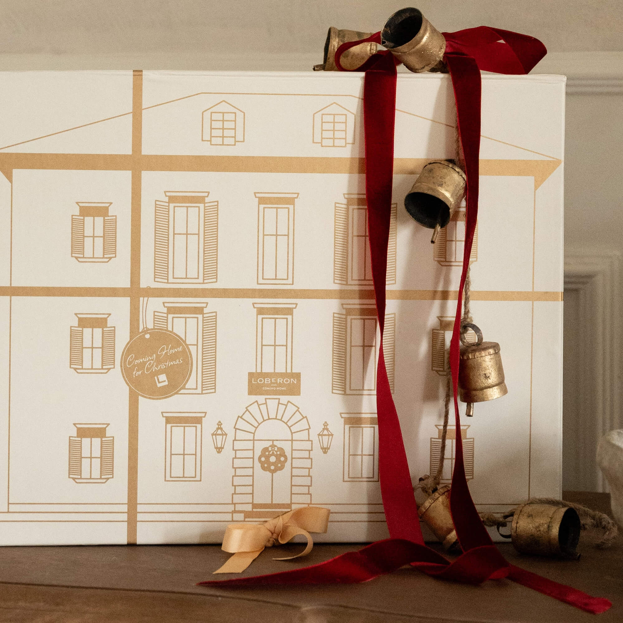 Decoratief setje gouden bellen aan rode lint met beige kerstcadeaudoos