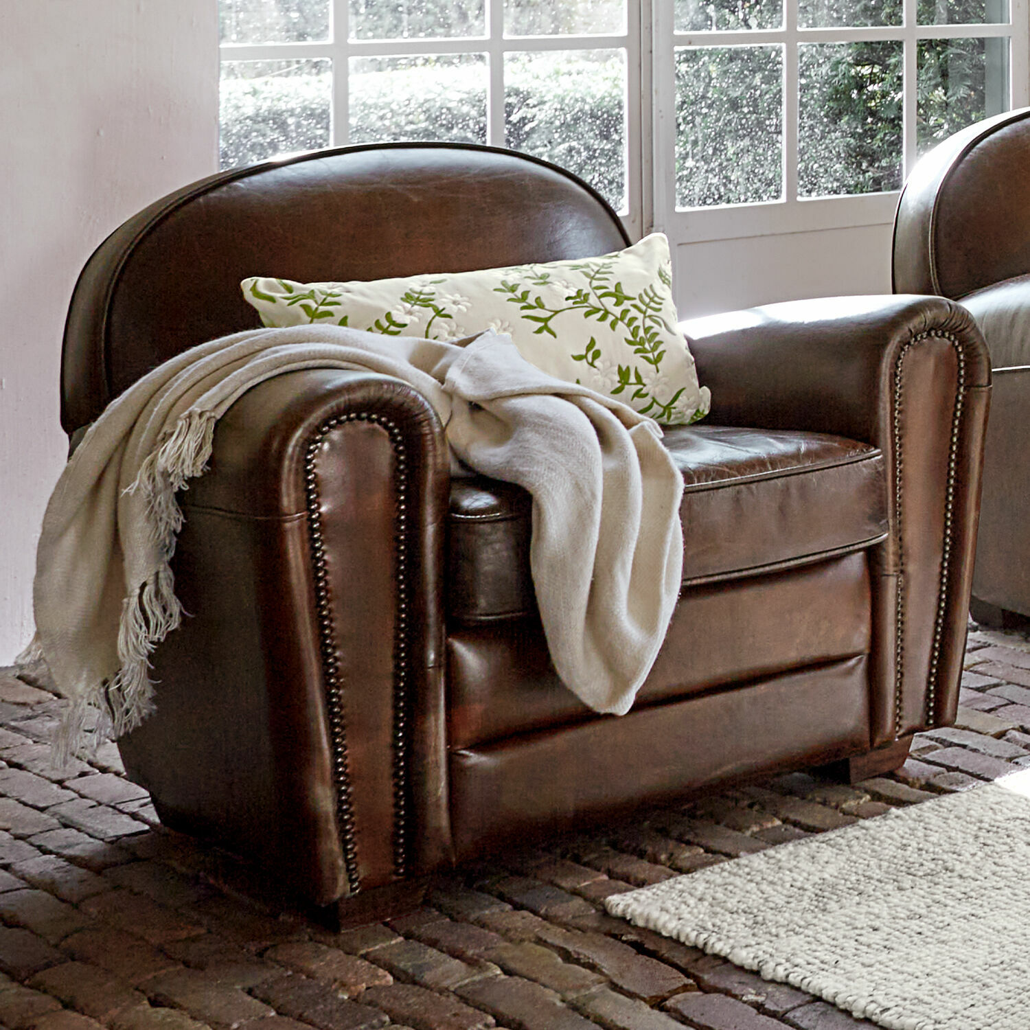Bruine leren fauteuil met witte deken en groen patroon kussen in lichte kamer