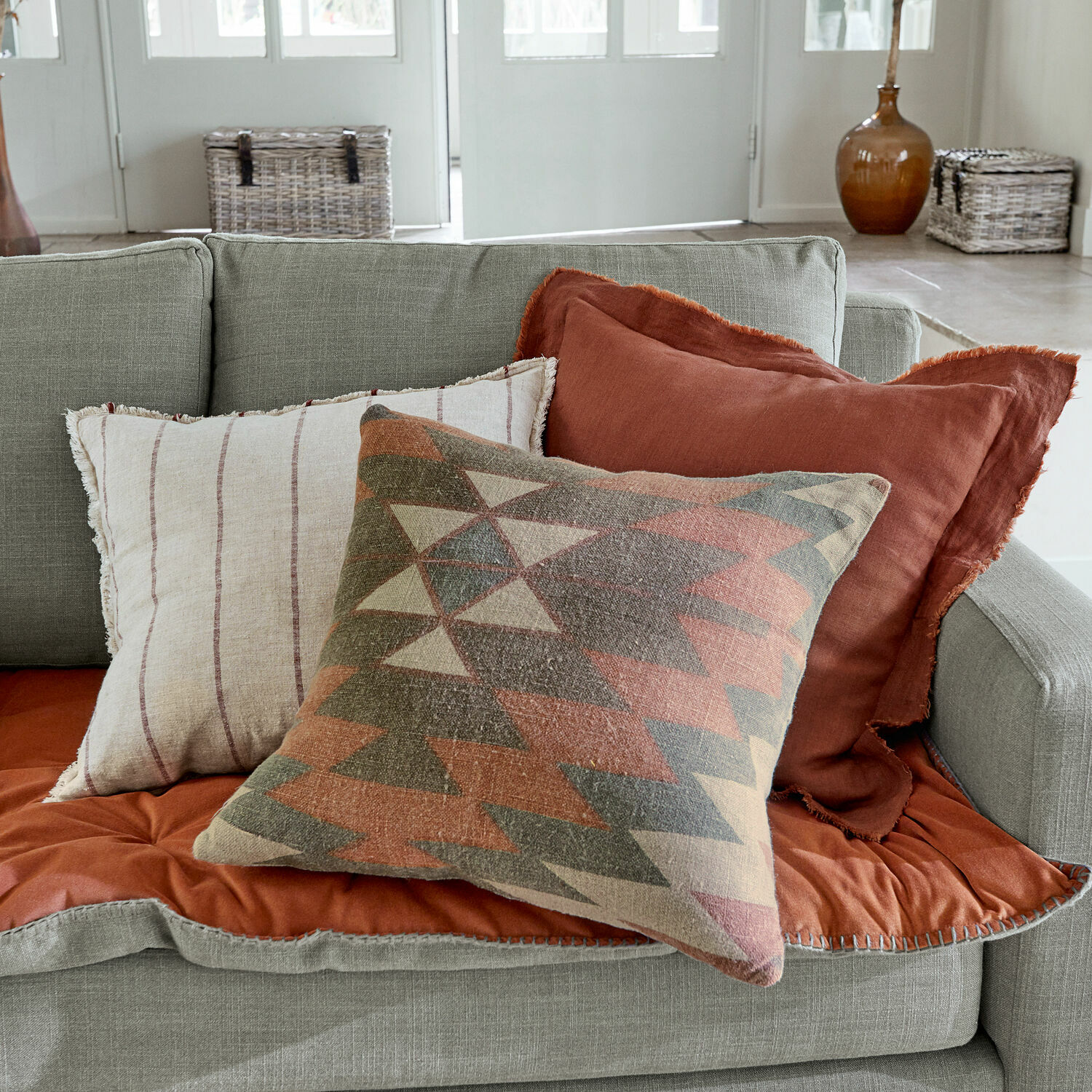 Set van drie decoratieve stoffen kussens in warme tinten op een grijze bank