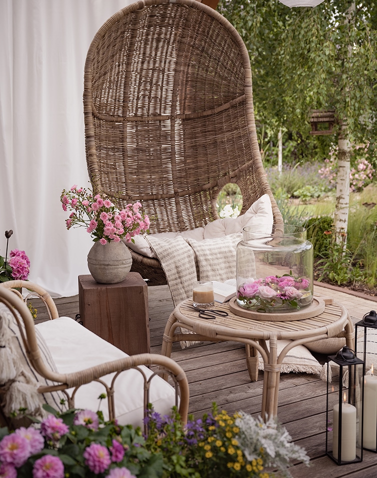 Gezellige zithoek met rotan stoel en bijzettafel op terras met bloemen en kaarsen