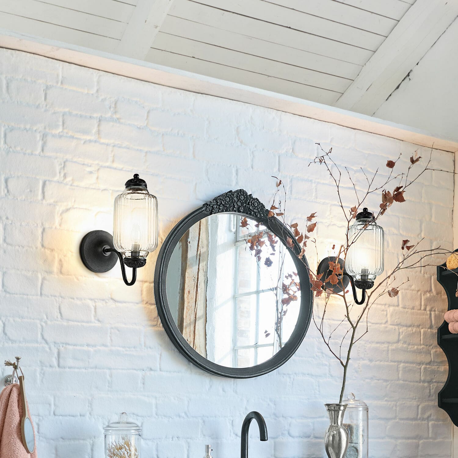 Ronde spiegel met zwarte lijst en bloemdecoratie aan witte bakstenen muur met wandlampen