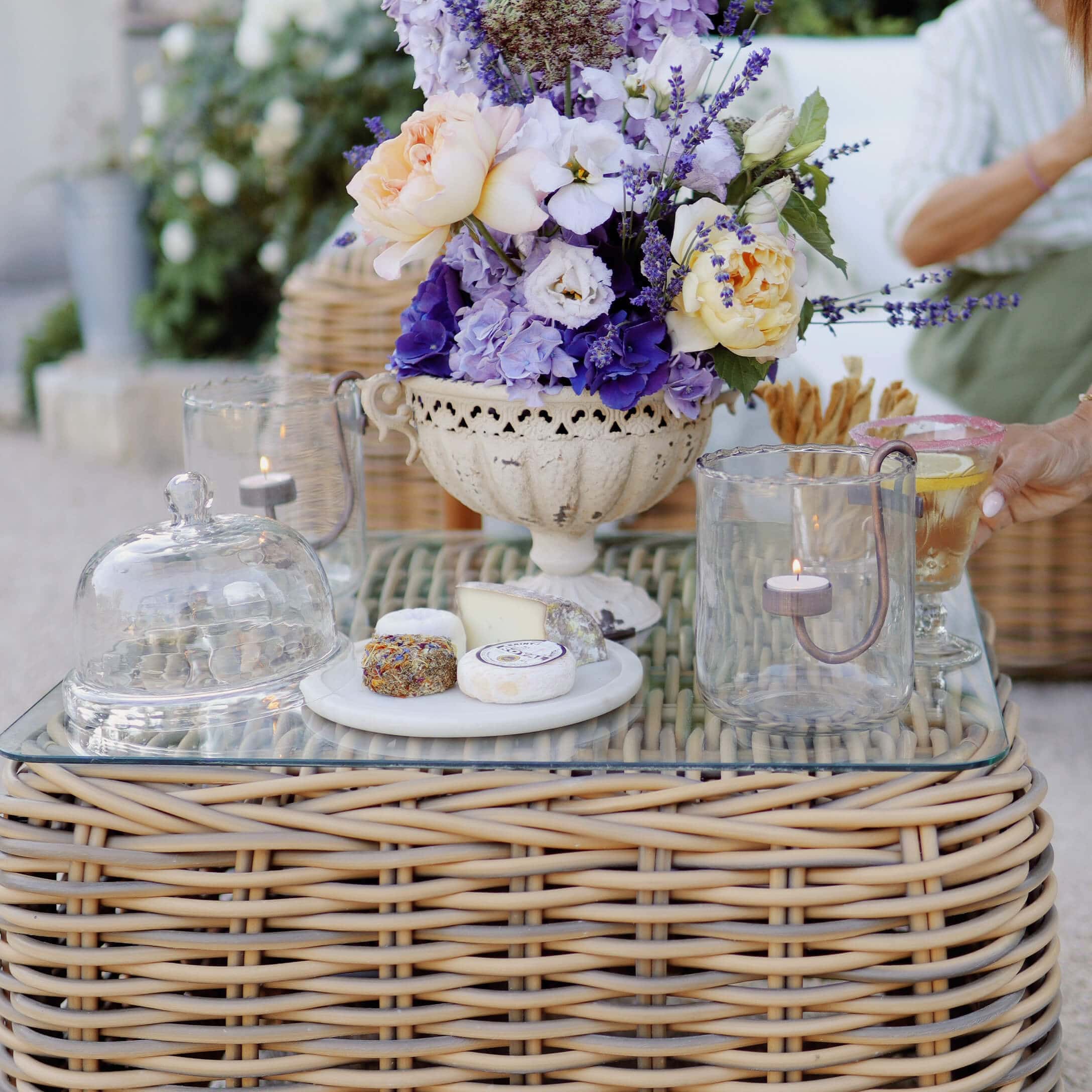 Decoratief boeket van lavendel en rozen in witte keramische vaas op rotan tafel met kaas en glas