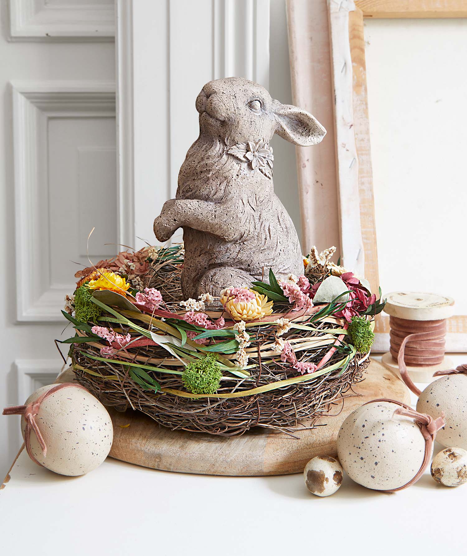 Decoratief betonnen konijn in nest met gedroogde bloemen en decoratieve eieren voor lente