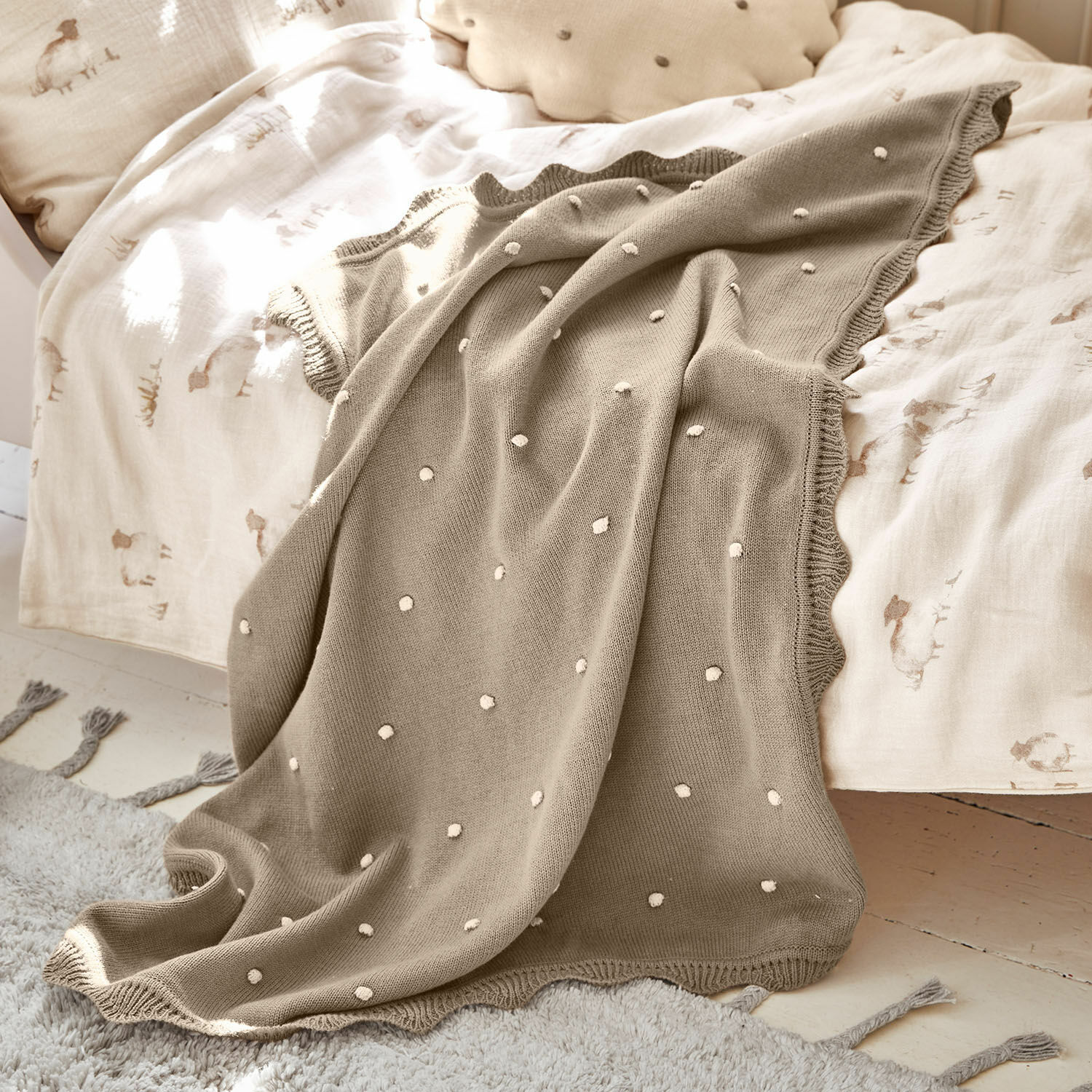 Beige gebreide deken met witte stippen op licht beddengoed, zachte en decoratieve plaid