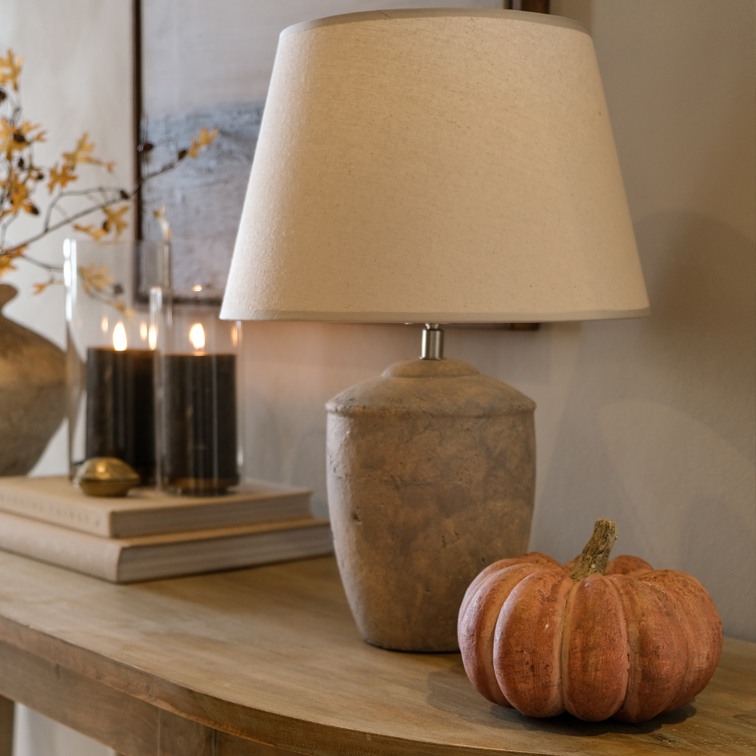 Tafellamp met beige kap en stenen voet op houten tafel met pompoendecoratie
