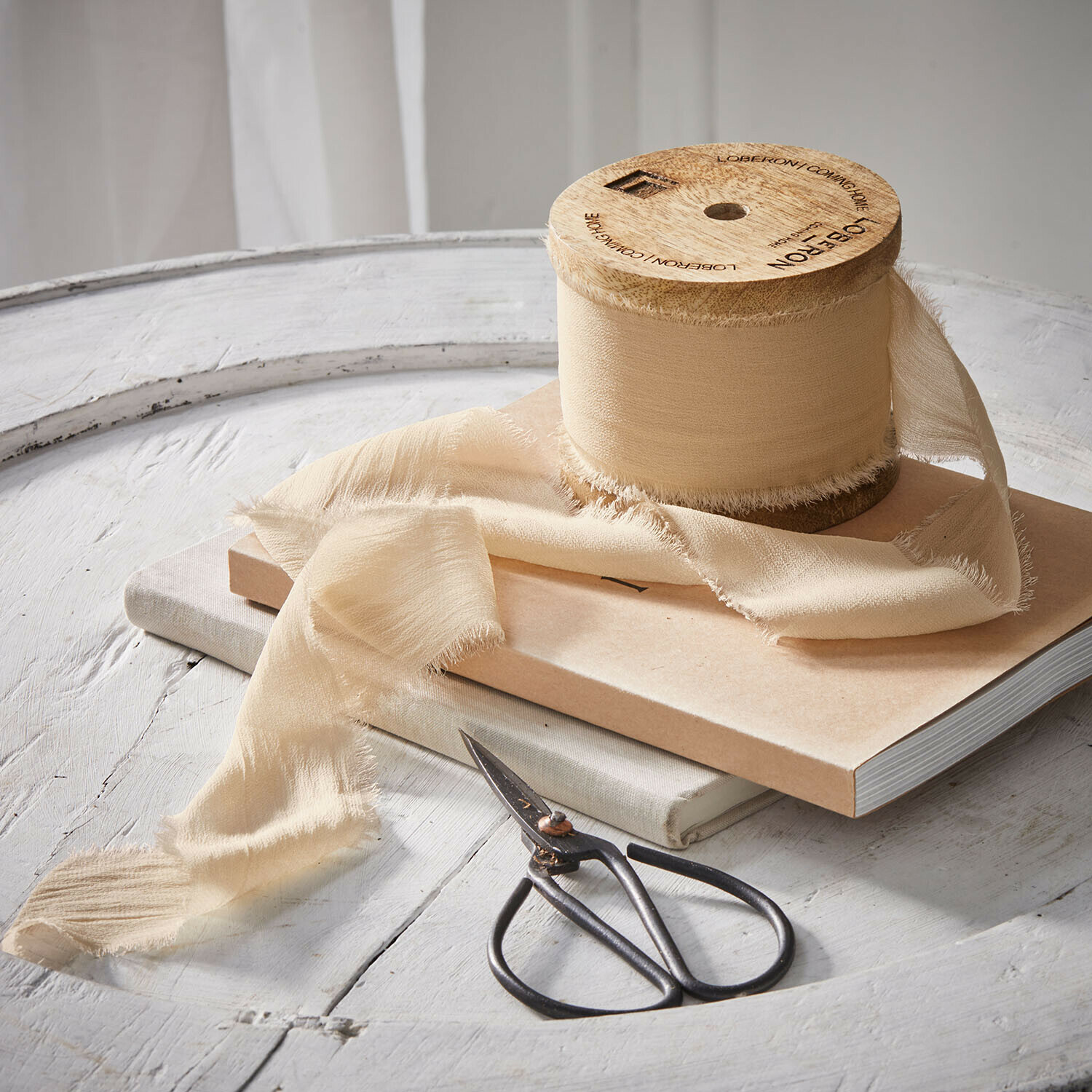 Beige lint met franjes op houten klos naast schaar op witte tafel voor decoratie en handwerk