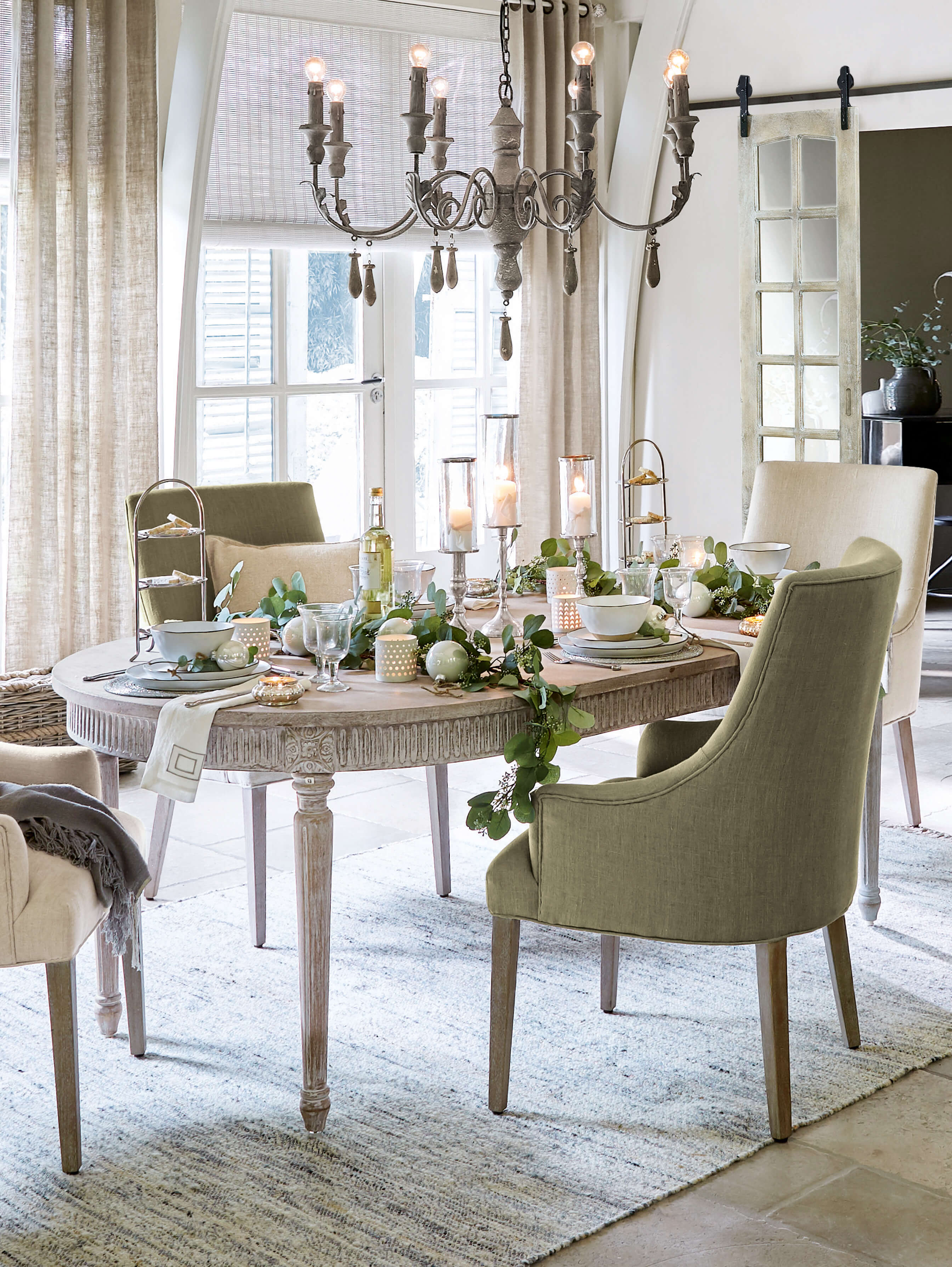 Eetkamer met houten tafel en groene gestoffeerde stoelen, feestelijke decoraties en kaarslicht
