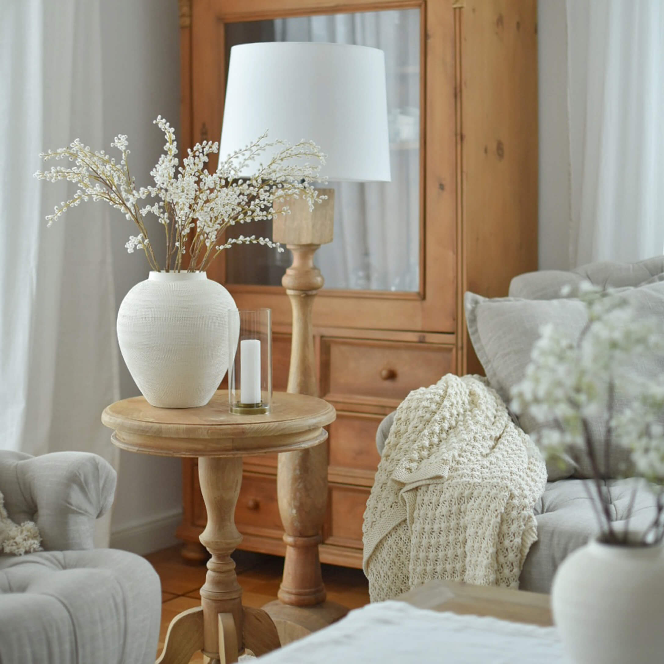 Lichte houten tafel met witte keramische vaas en lamp in gezellige woonkamer met beige deken