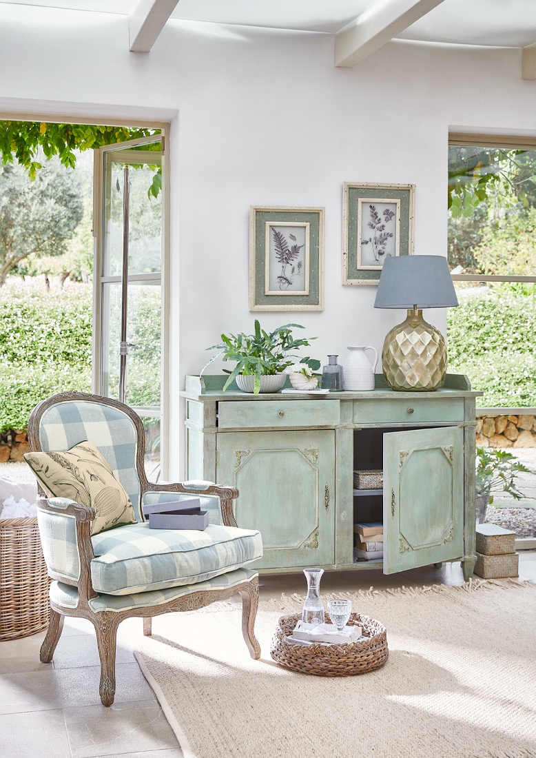 Vintage houten dressoir in muntgroen met decoratieve lamp en planten in lichte woonkamer met geruite stoel