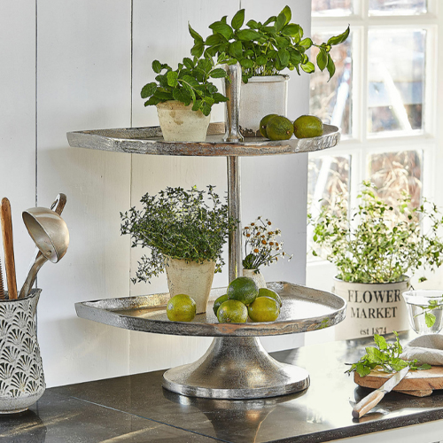 Tweeledig zilverkleurig metalen etagère met groene planten en limoenen op keukenblad