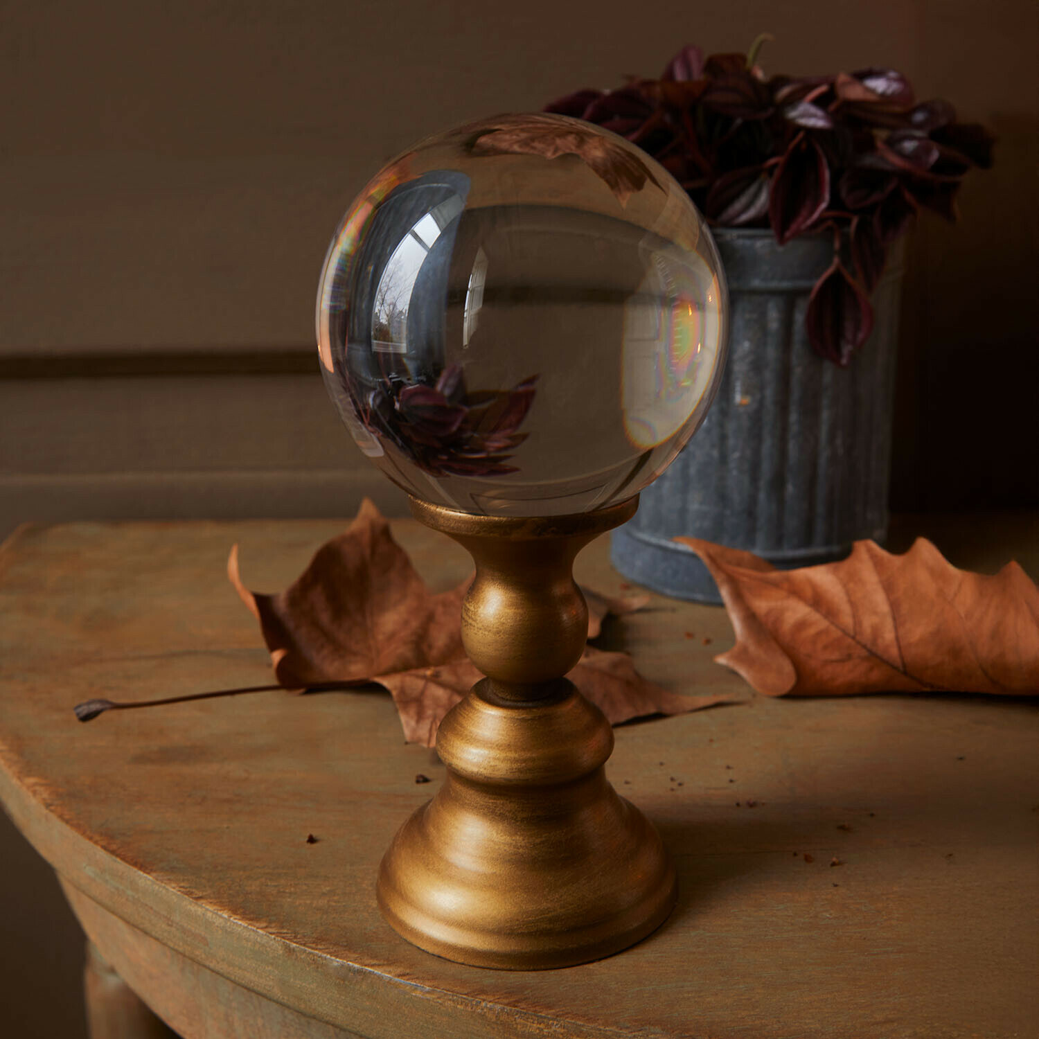 Glazen bol op gouden metalen standaard op houten tafel met droge bladeren en bloempot