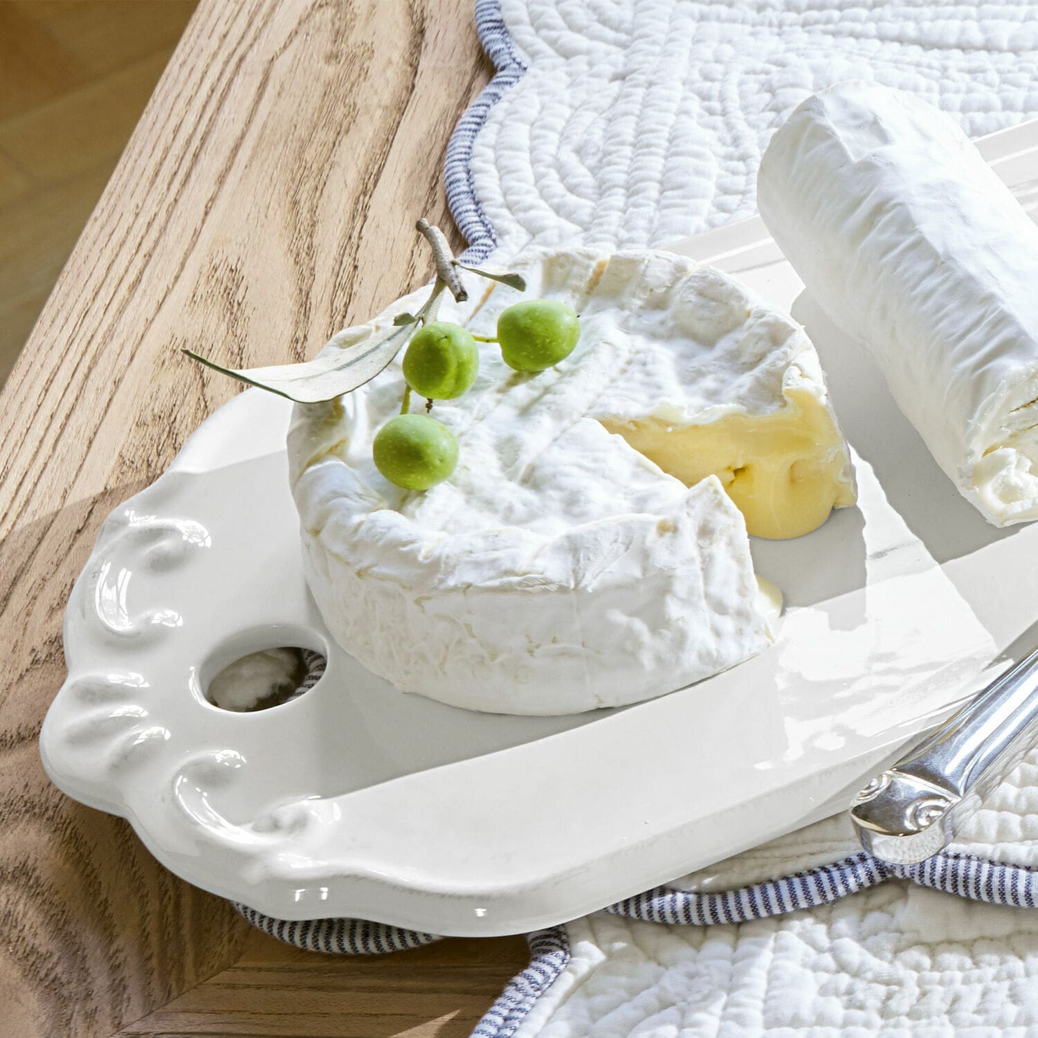 Witte keramische schaal met decoratief handvat, camembert en geitenkaas op houten tafel