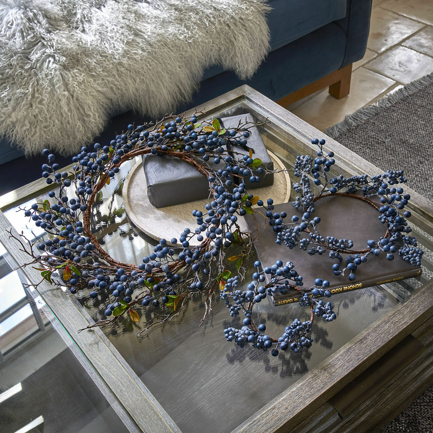 Decoratieve kransen met blauwe bessen op glazen tafel in woonkamer met zachte deken