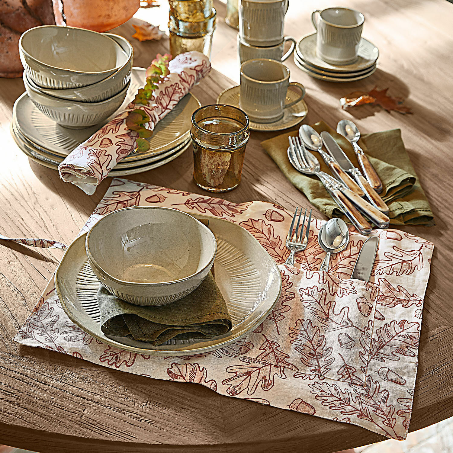 Beige keramisch servies met borden en kommen op houten tafel met decoratief servet met bladeren