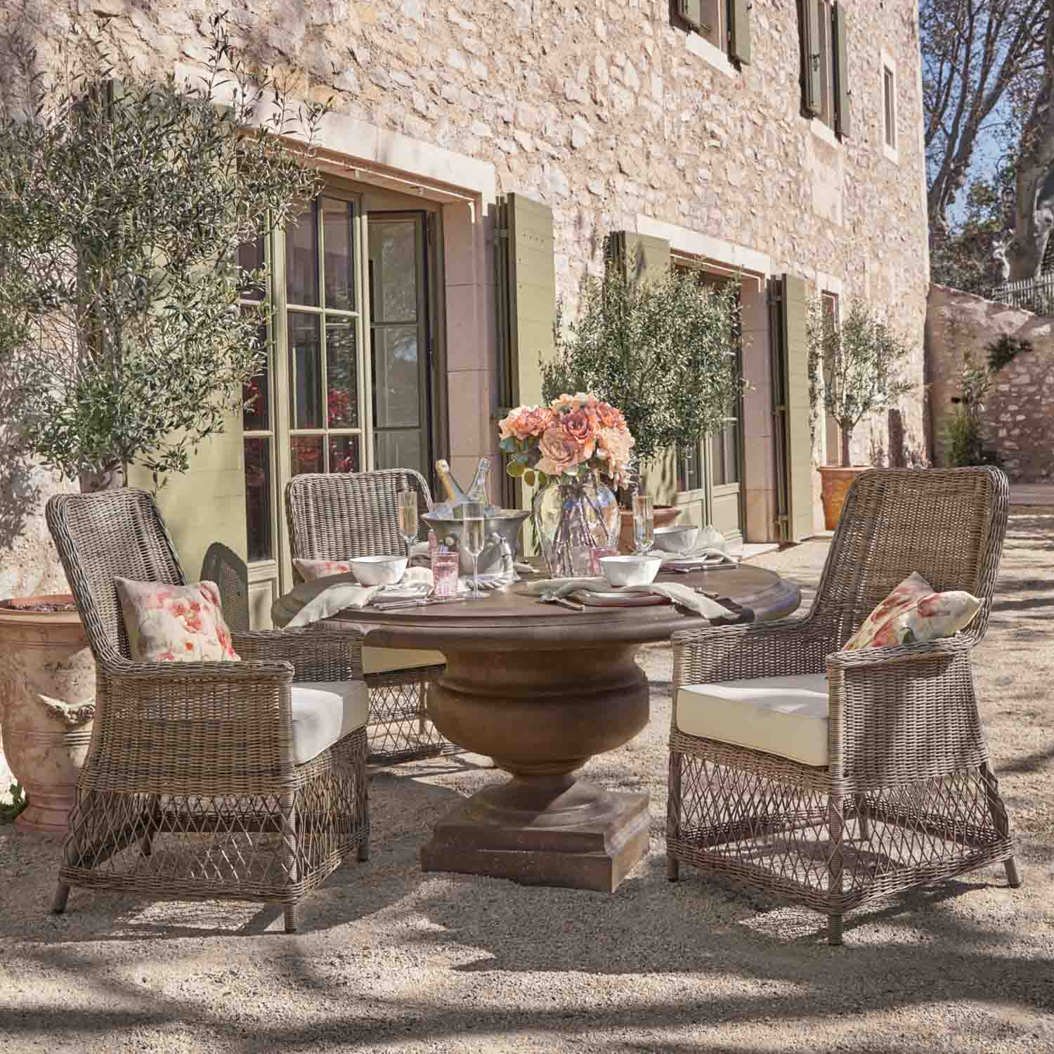 Ronde stenen tuintafel met rotan stoelen en bloemen op zonnig terras buiten