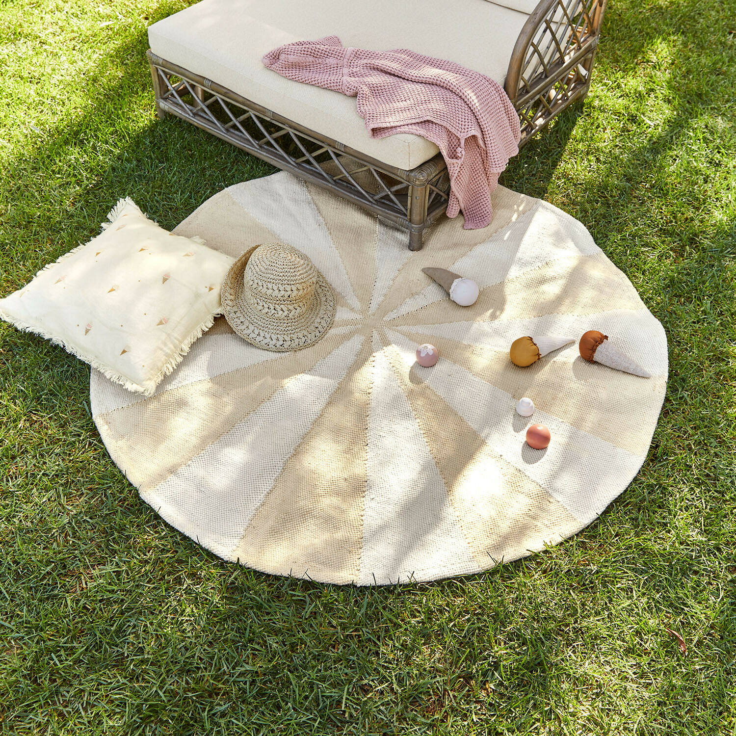 Ronde vloerkleed van natuurlijk materiaal in beige-crèmekleuren op gras met kussen en strohoed