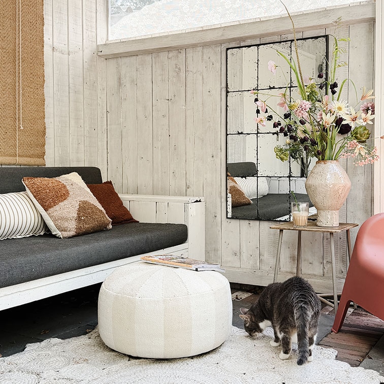 Gezellige woonkamer met witte houten wand, grijze bank, witte poef en bloemen op houten tafeltje