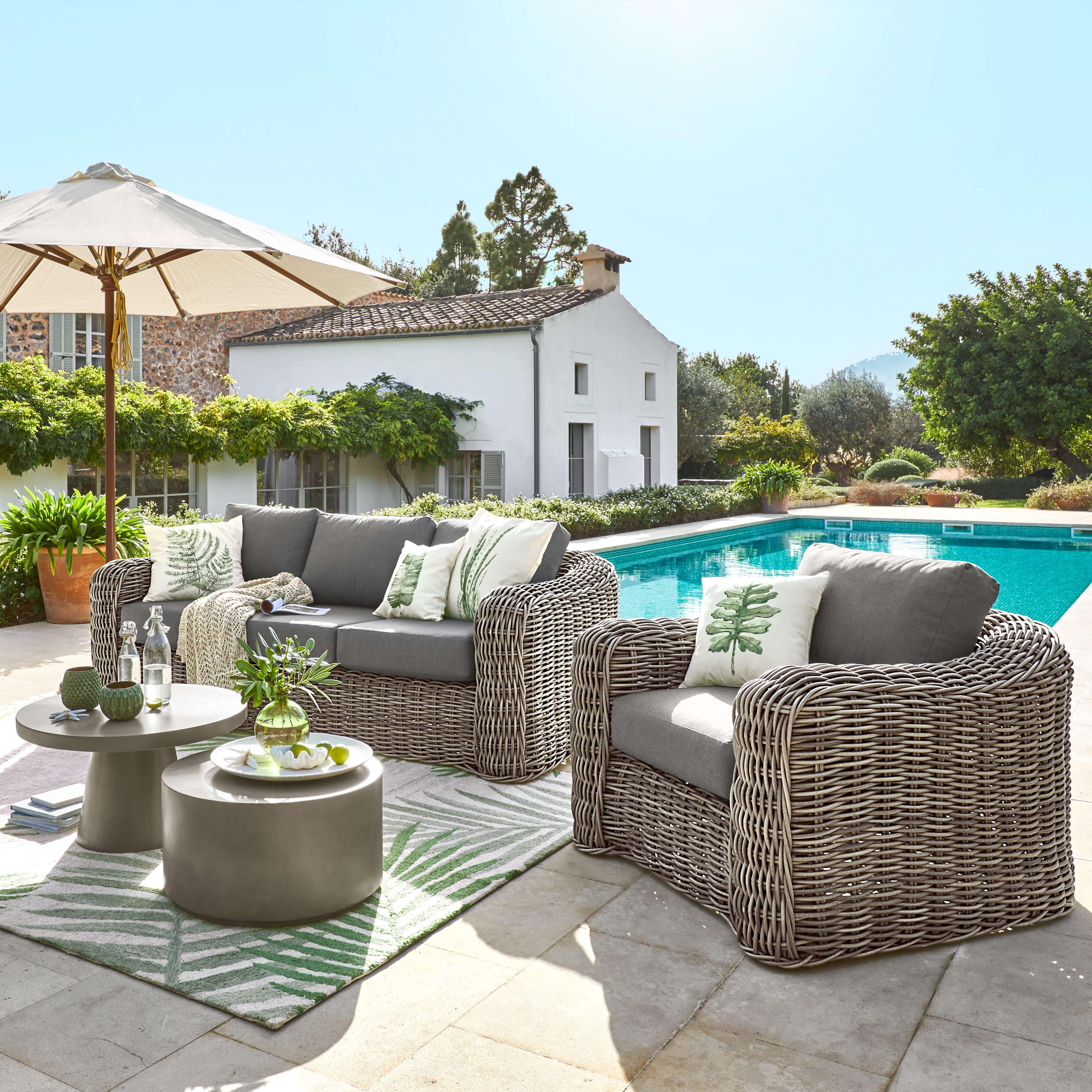 Tuinmeubelset van grijs rattan met kussens en bijzettafels bij het zwembad in de tuin