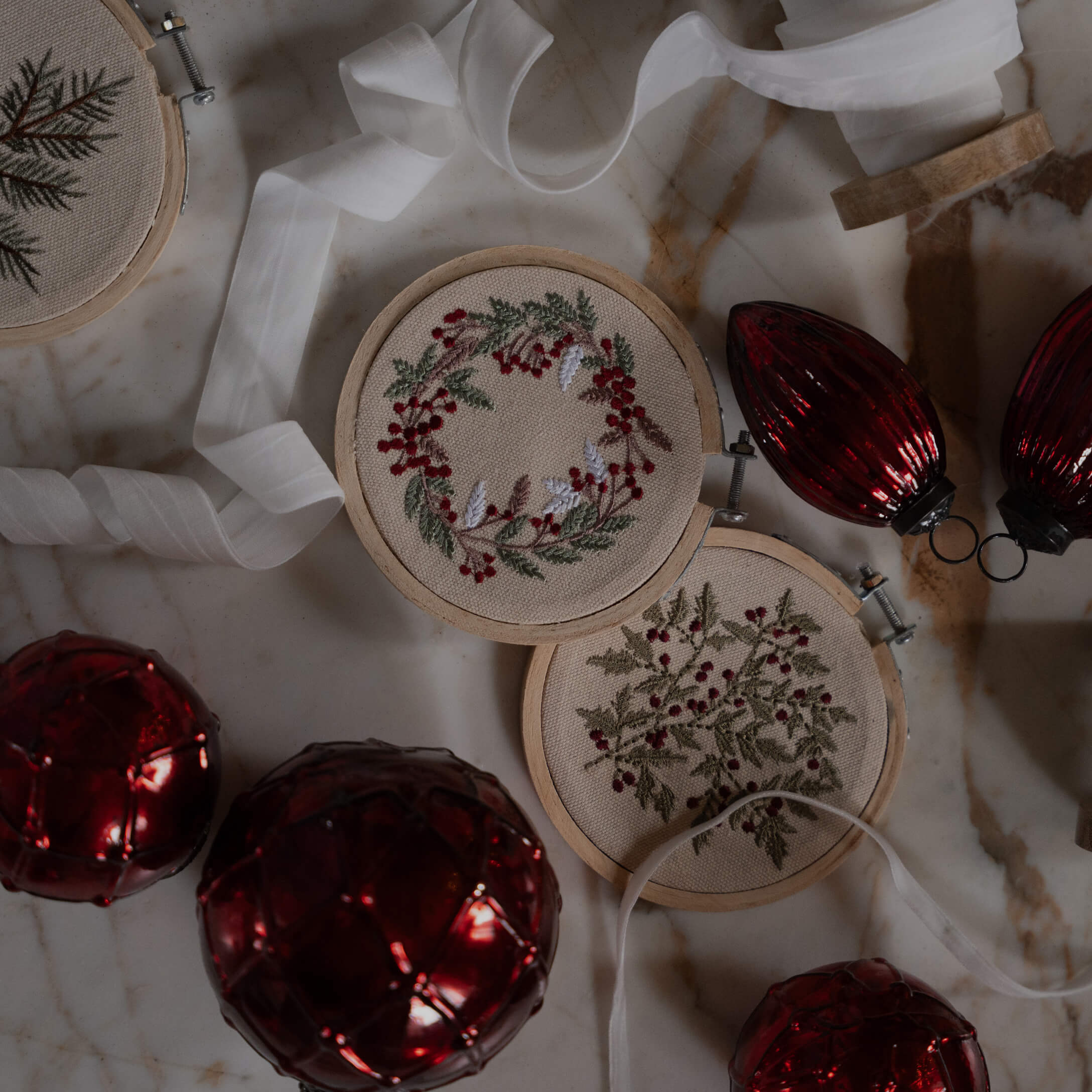 Twee borduurringen met rode bessen en groene bladeren op beige stof, kerstdecoratie