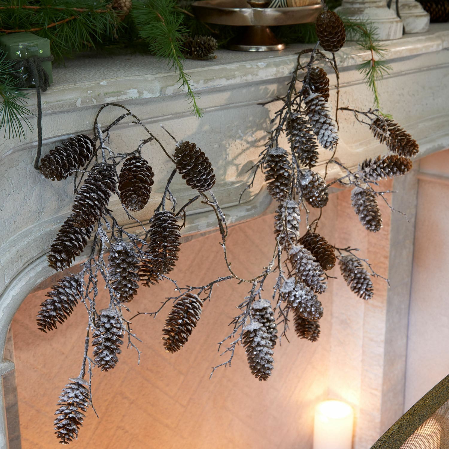Guirlande Soralaith Takken met besneeuwde dennenappels aan een stenen open haard, natuurlijke kerstdecoratie