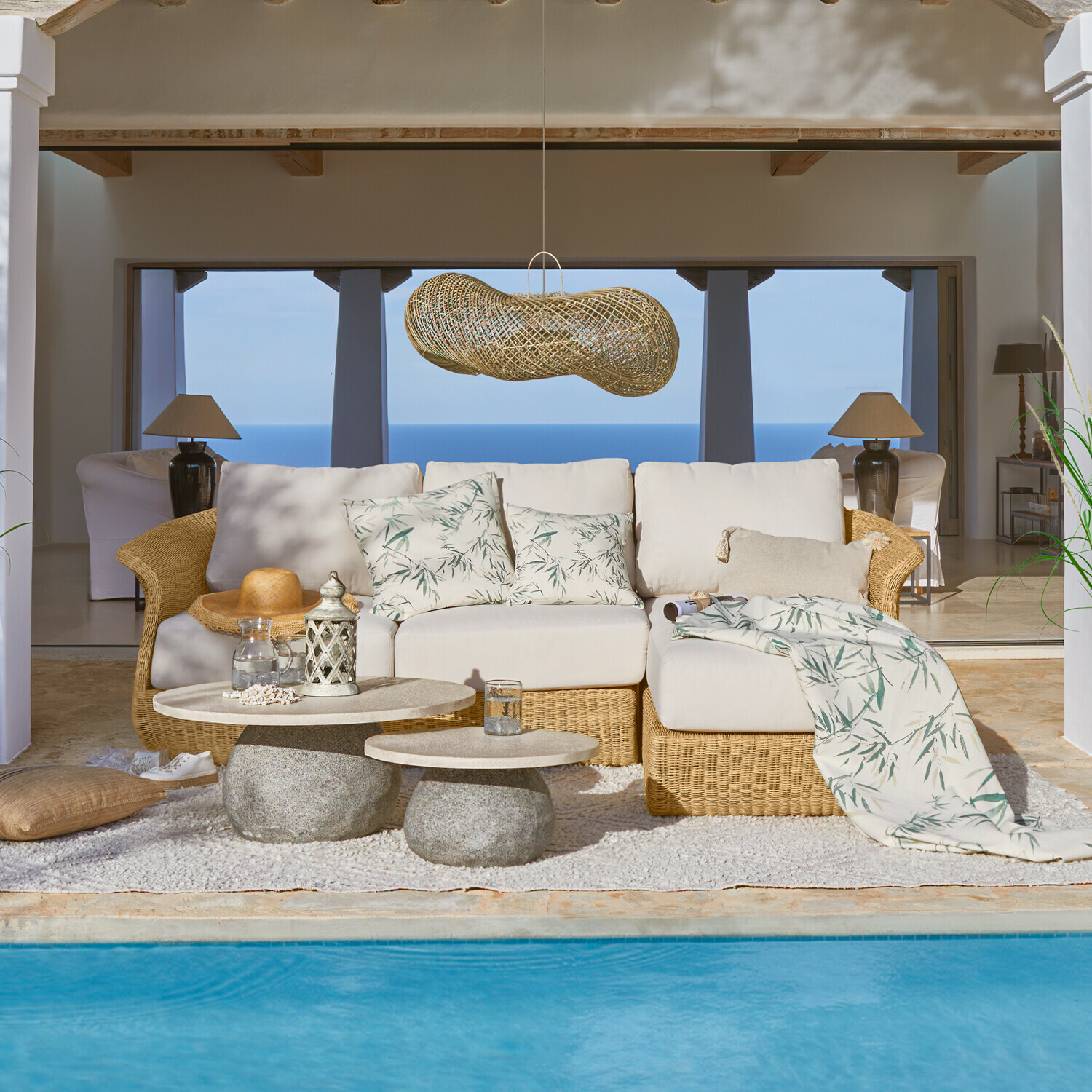 Comfortabele rotan bank met lichte kussens met bladmotief bij zwembad met zeezicht