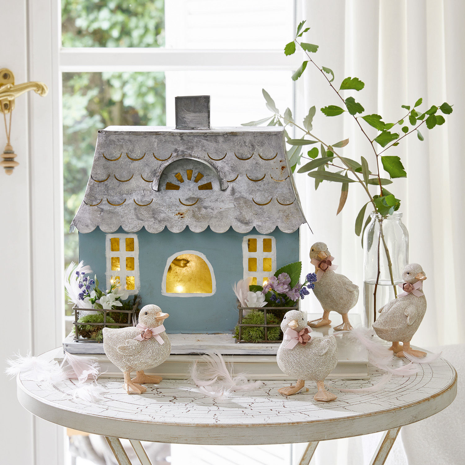 Decoratief blauw metalen huis met vier witte eendjes en bloemen op een ronde witte tafel