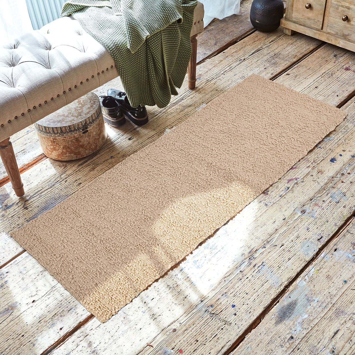 Beige vloerkleed van zacht materiaal op houten vloer in gezellige ruimte met bank en groene deken