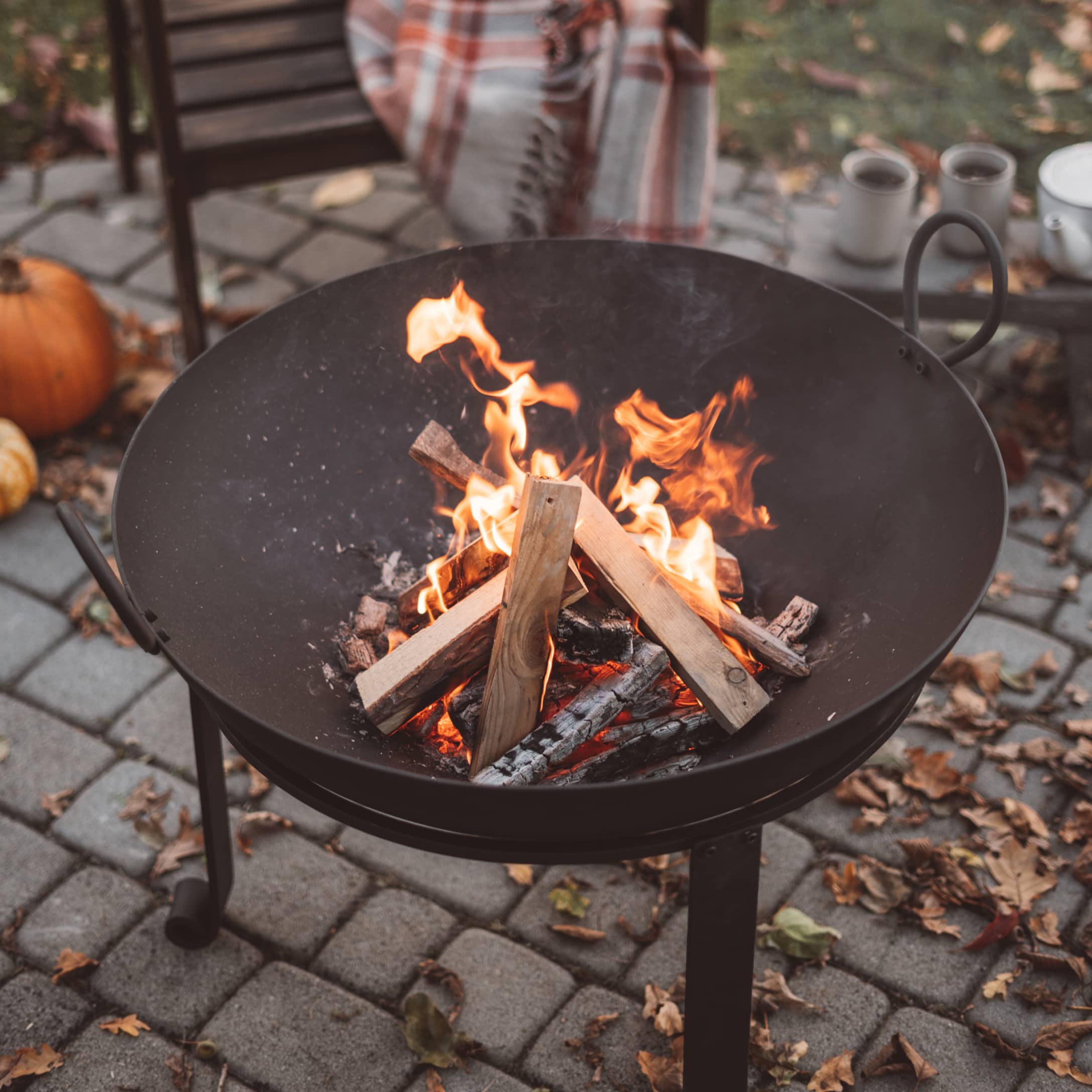 Zwarte metalen vuurkorf met brandend hout op een betegeld terras in de tuin