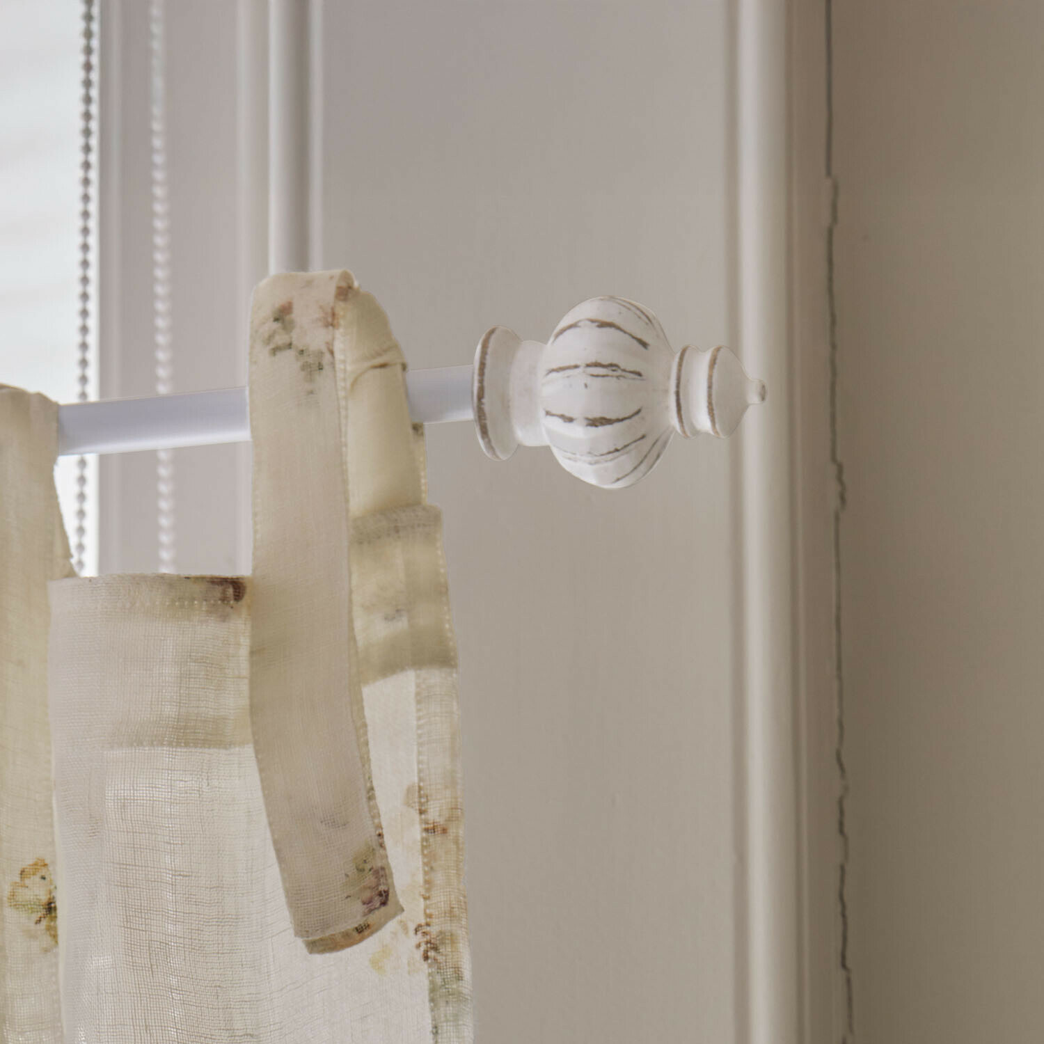 Witte houten eindkap voor gordijnroede met crèmekleurige, lichte stofgordijn bevestigd