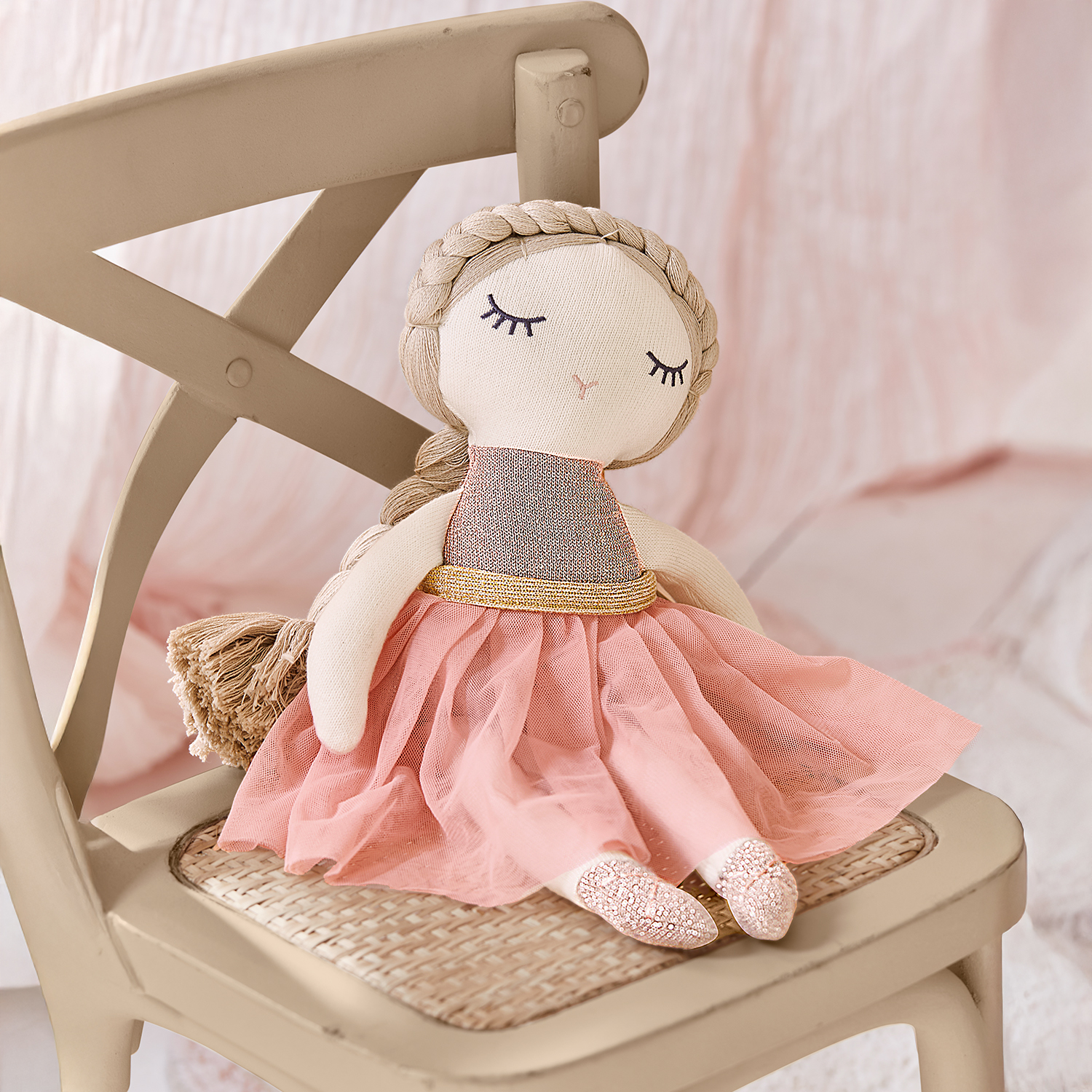 Stoffen pop met roze jurk en gouden riem zittend op een beige stoel, kinderspeelgoed