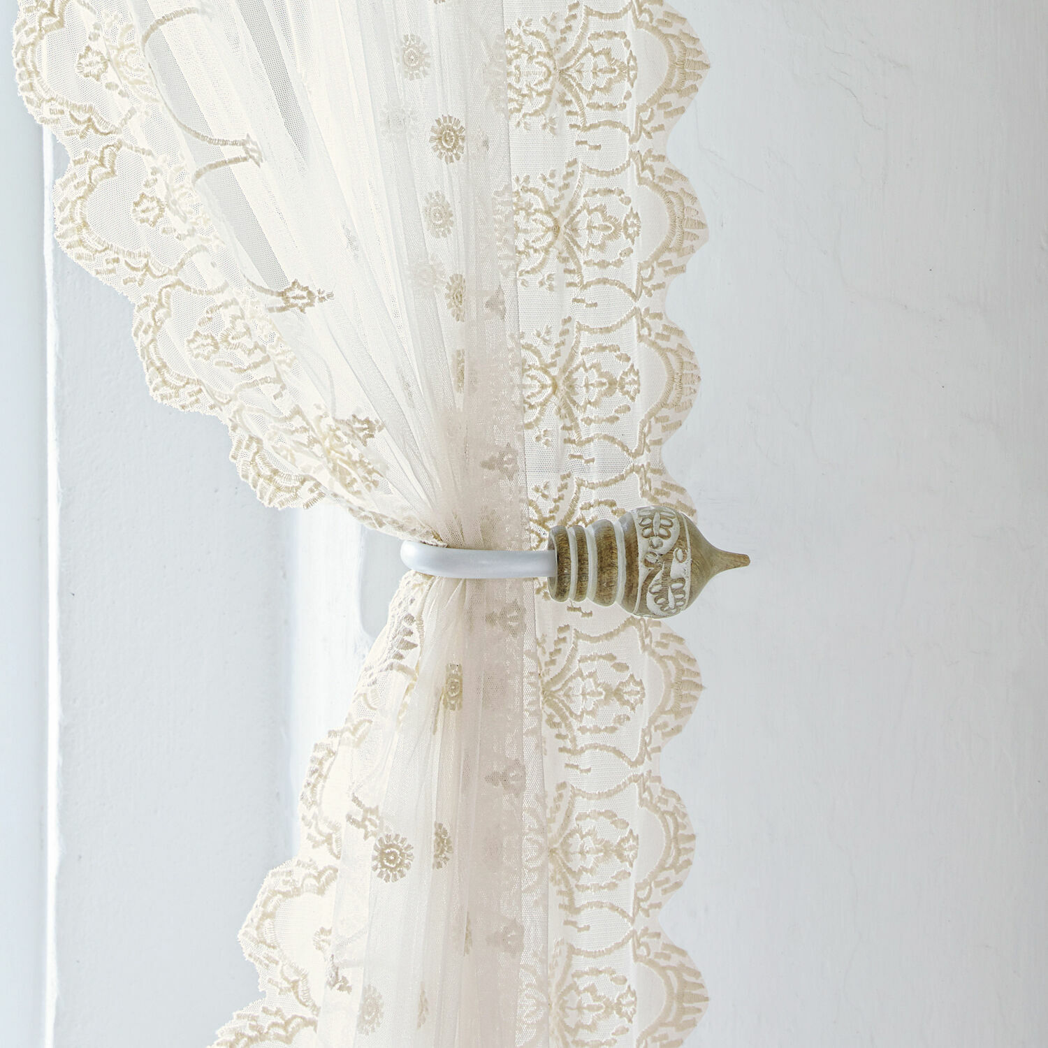 Embrasse set van 2 Talon Beige kanten gordijn met decoratieve metalen houder tegen lichte muur, raamdecoratie
