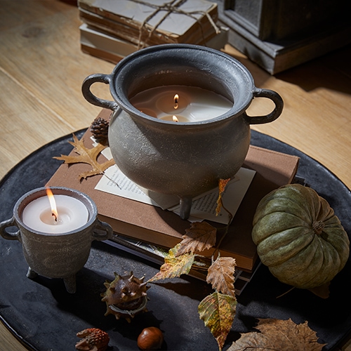 Kaars in grijs keramisch vat met handvatten op houten tafel met herfstdecoratie