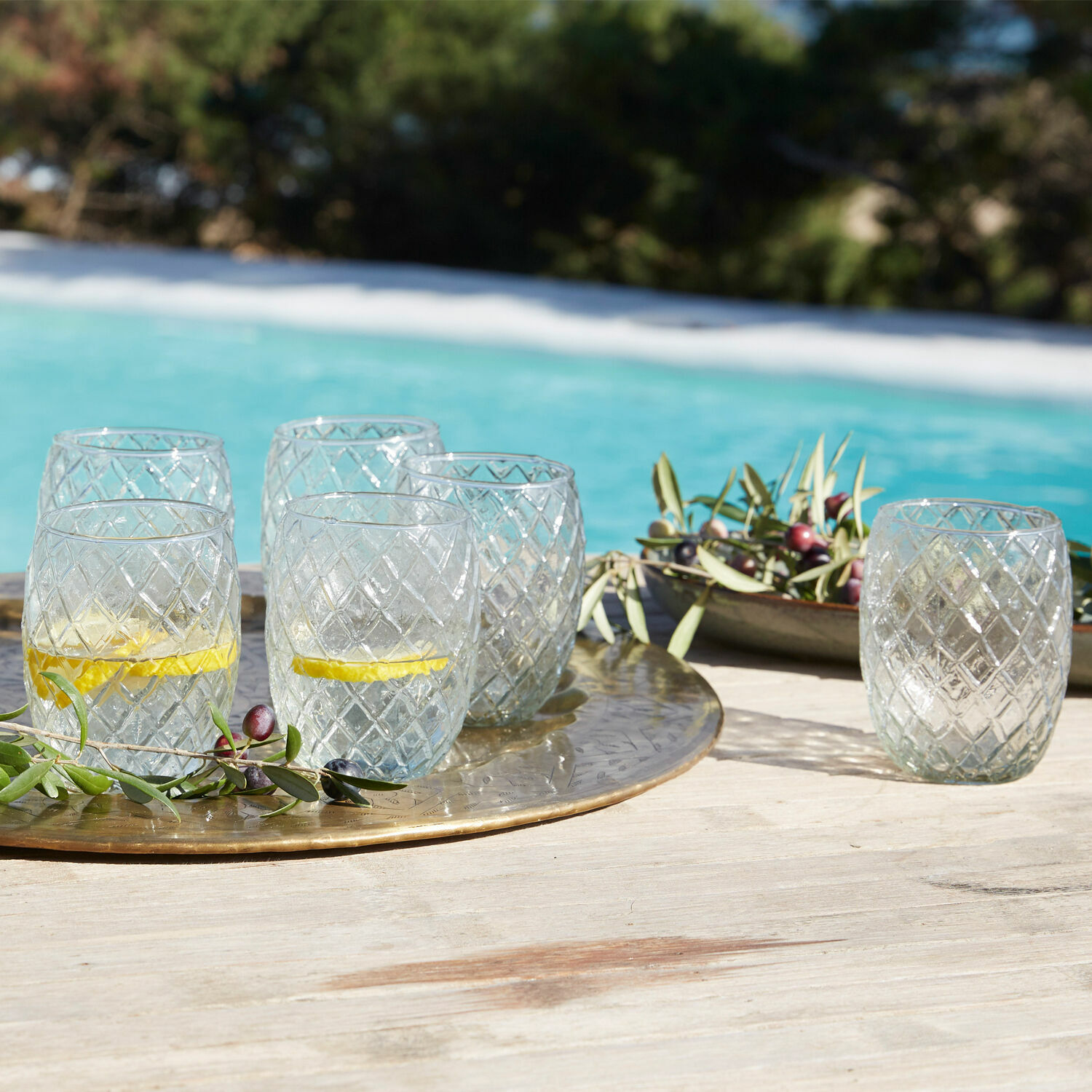 Glazen van helder glas met diamantpatroon op gouden dienblad bij het zwembad