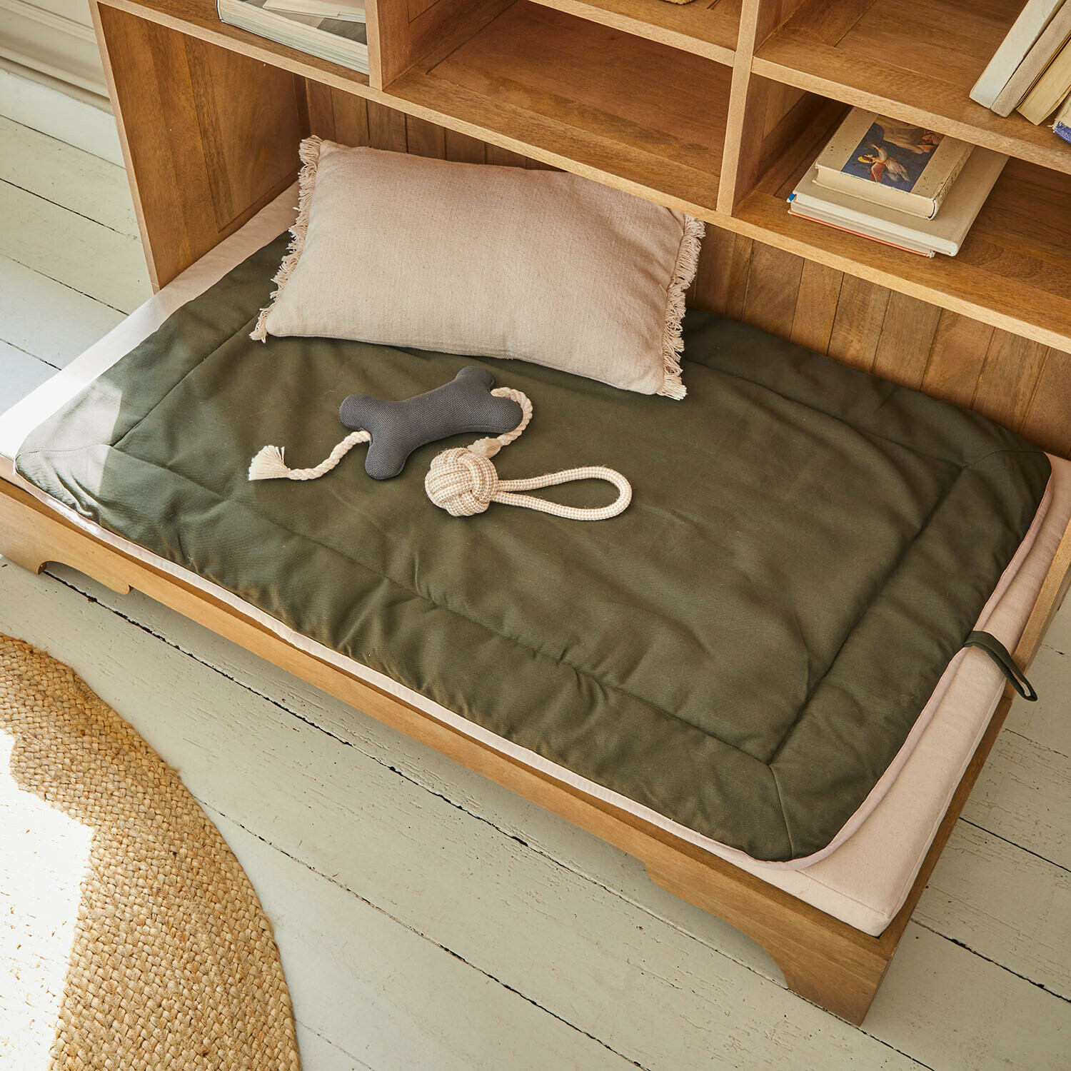 Kussen en groene stoffen matras op houten bed met hondenspeelgoed in natuurlijke omgeving