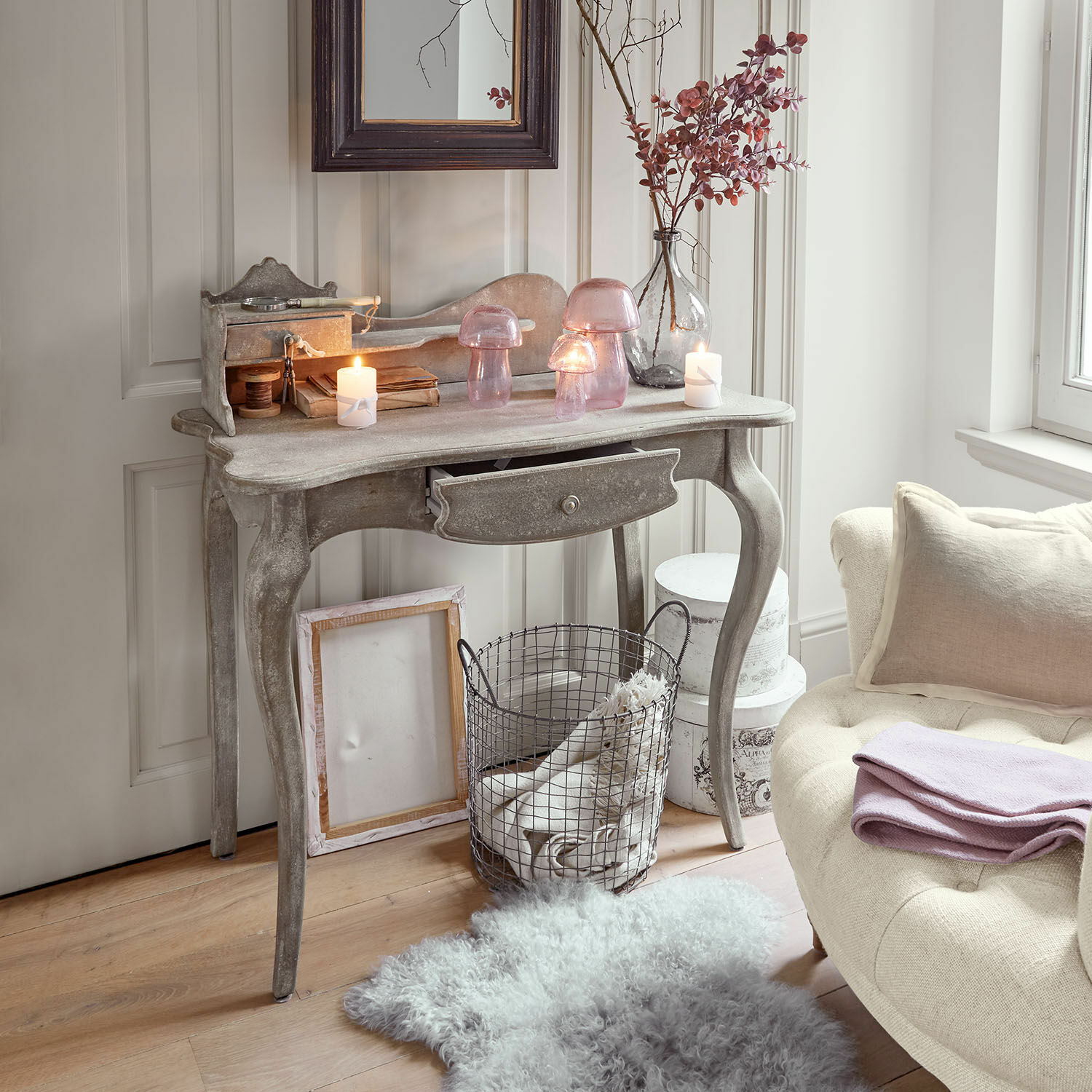 Grijze houten console met lade, versierd met roze glazen lampen en kaarsen in een gezellige kamer