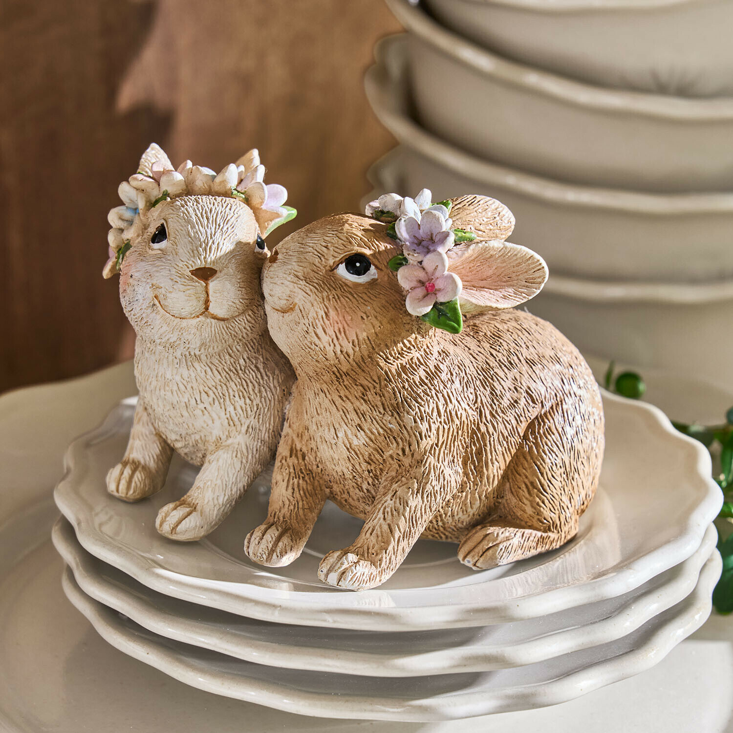 Twee keramische konijnenfiguren in beige en wit met bloemenkransen op witte borden