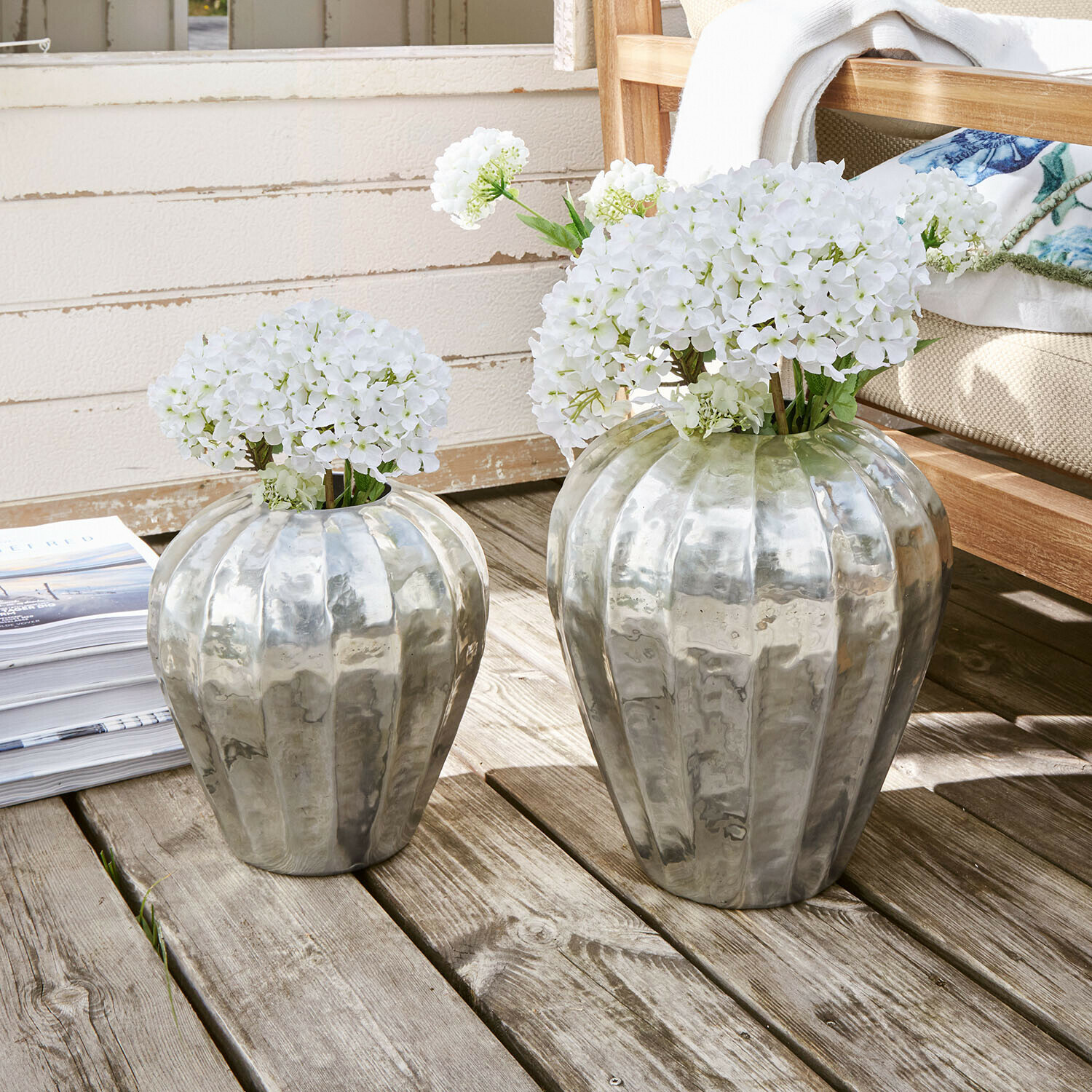 Twee zilverkleurige metalen vazen met witte bloemen op houten terras, interieurdecoratie