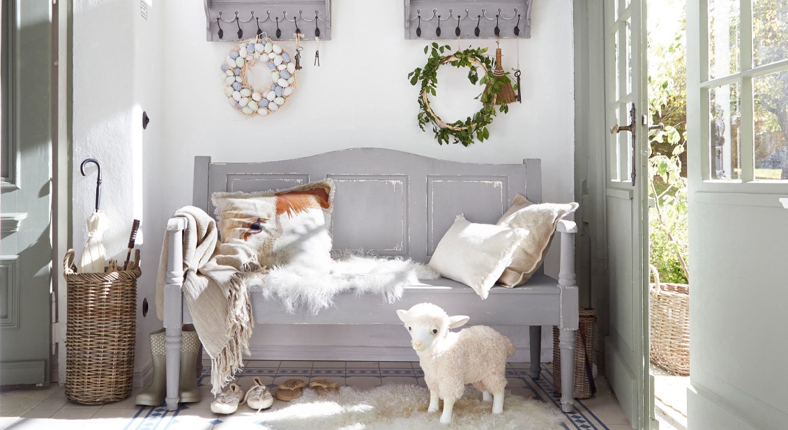 Grijze houten bank in shabby chic stijl met kussens en zachte vacht in een lichte, gezellige ruimte