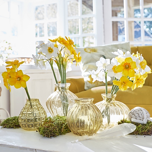 Set van vier doorzichtige glazen vazen met gele en witte bloemen op lichte tafel
