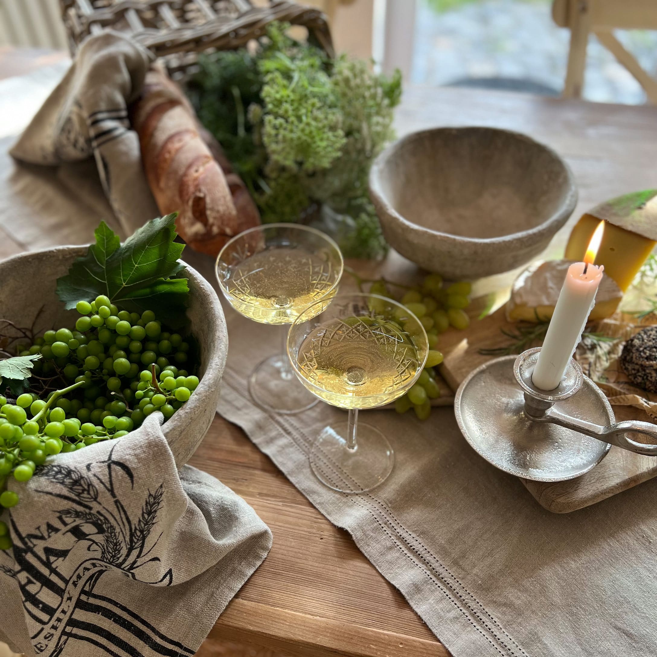 Rustieke tafel met stenen kommen, brandende kaars, glazen witte wijn, brood en groene druiven