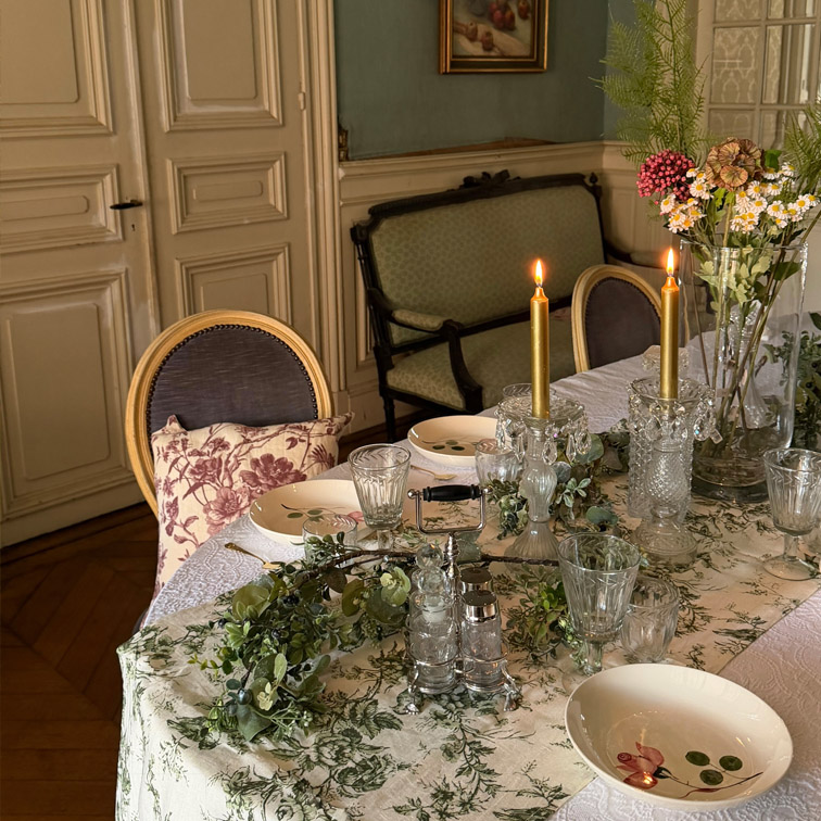 Elegante tafel met wit tafelkleed met groene patronen, brandende kaarsen en bloemen in een klassieke kamer