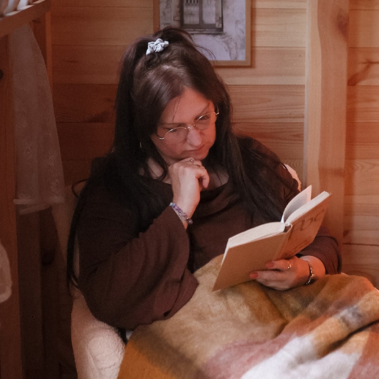 Vrouw leest boek onder zachte, meerkleurige deken in houten interieur, ontspannen moment thuis