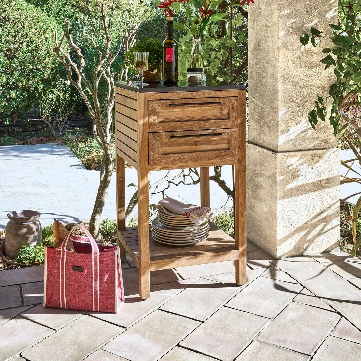 Houten kastje met zwart blad en twee lades op terras met servies en wijnfles