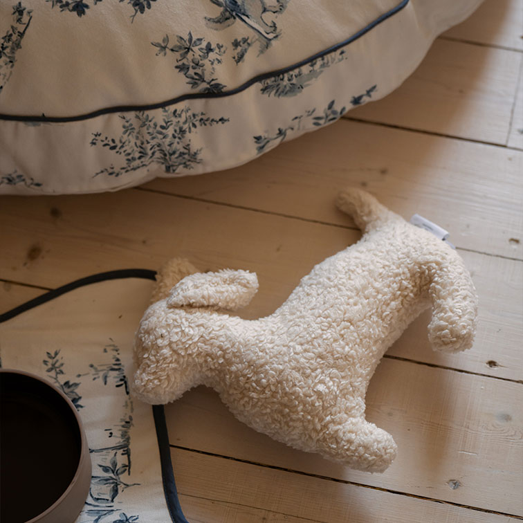 Zachte pluchen hondenvormige knuffel in crèmekleur op lichte houten vloer