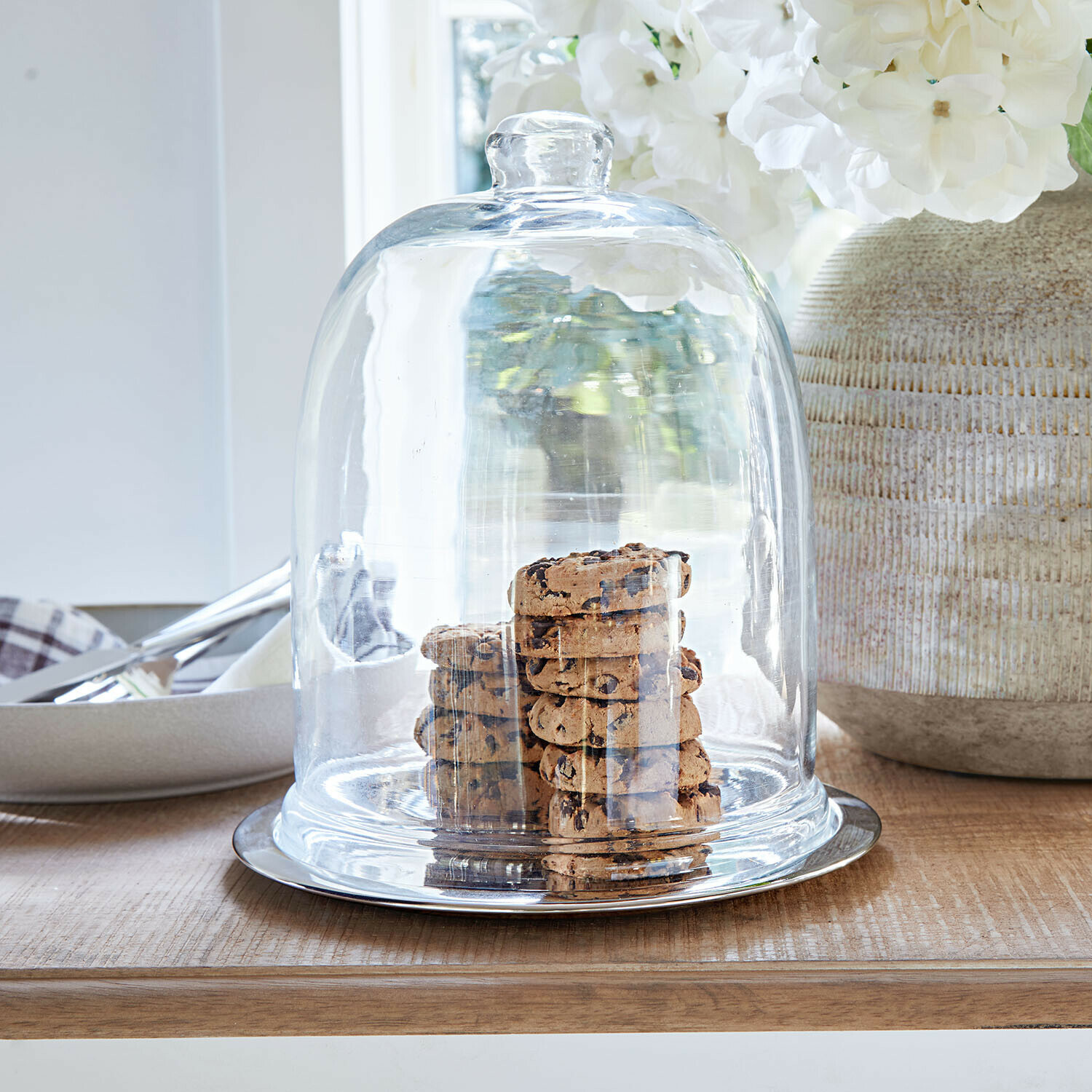 Glazen stolp met bordje Chardonne Glazen stolp met metalen onderplaat op houten tafel met chocoladekoekjes erin
